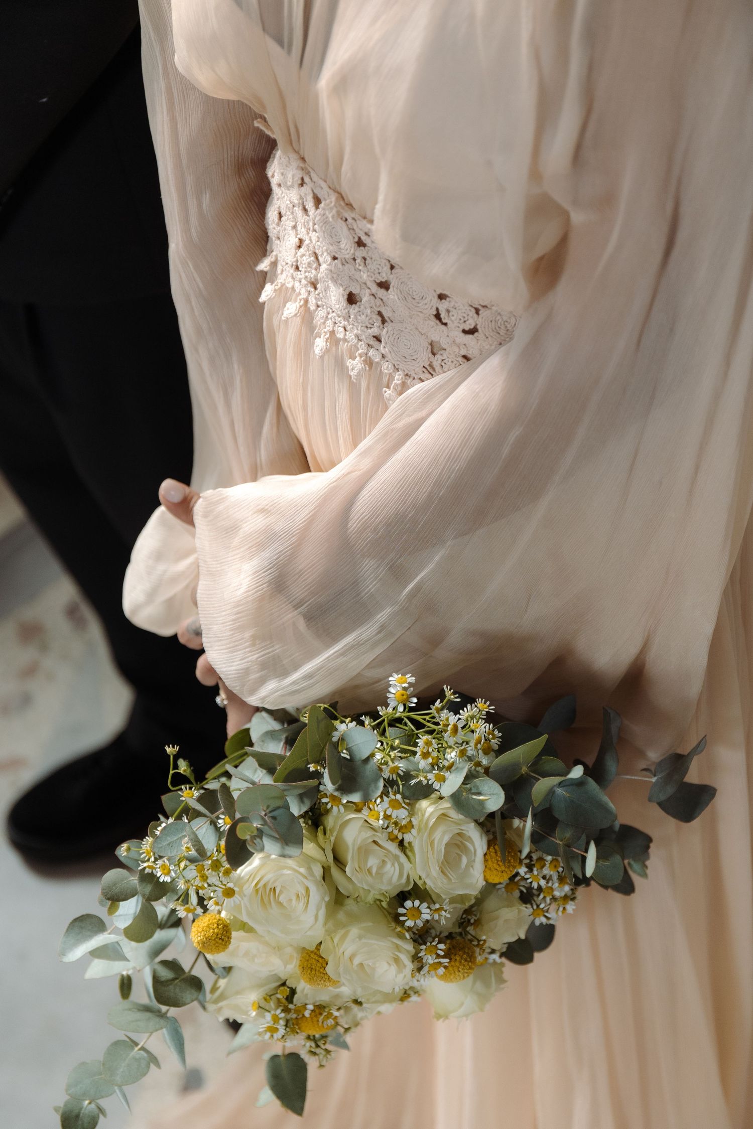 Close-up of a wedding dress detail with a white and yellow floral bouquet.