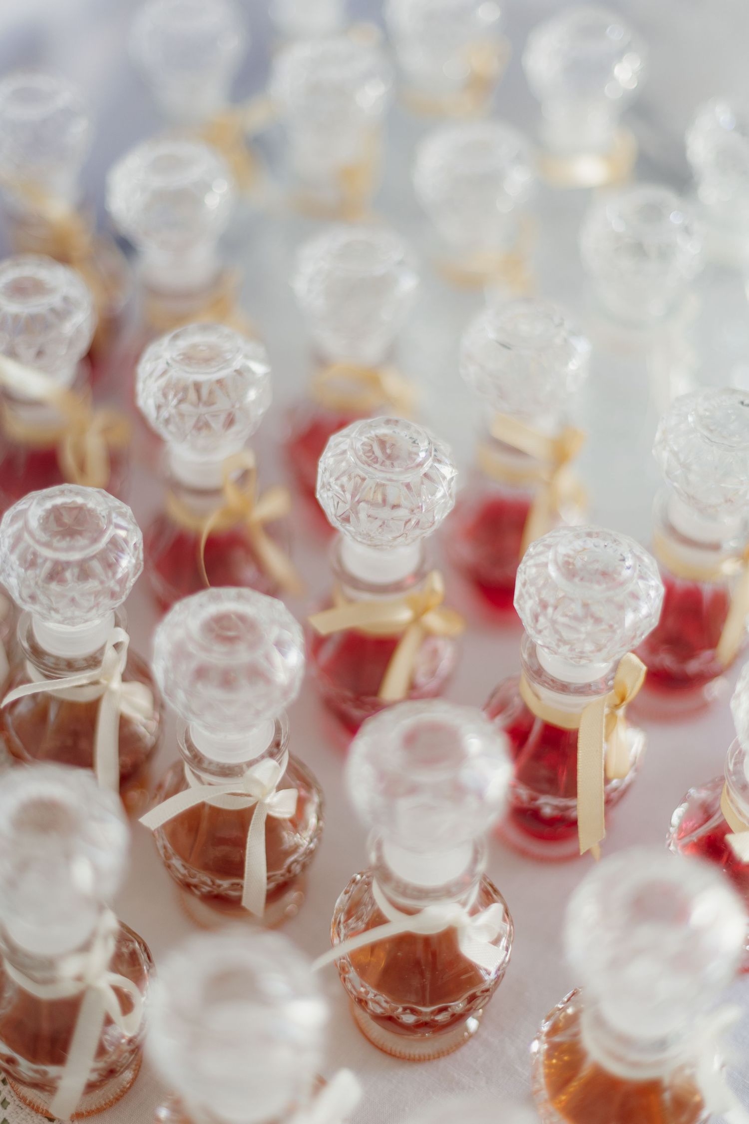 Small decorative glass bottles with stoppers arranged in rows containing pink and amber liquids.