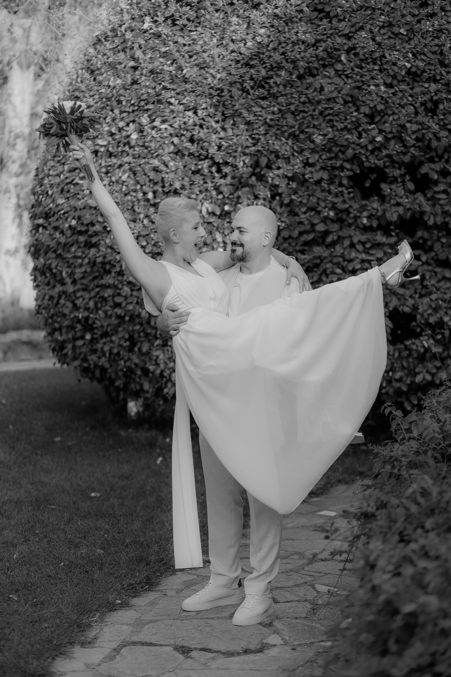 A graceful dance pose in white attire against a lush garden hedge backdrop.