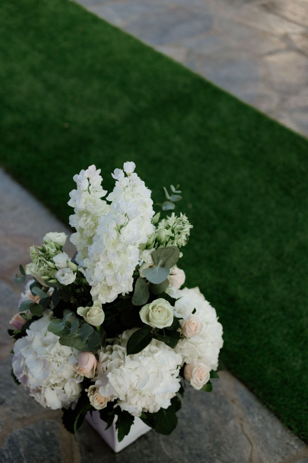 Elegant white floral arrangement with roses and hydrangeas on stone paving.