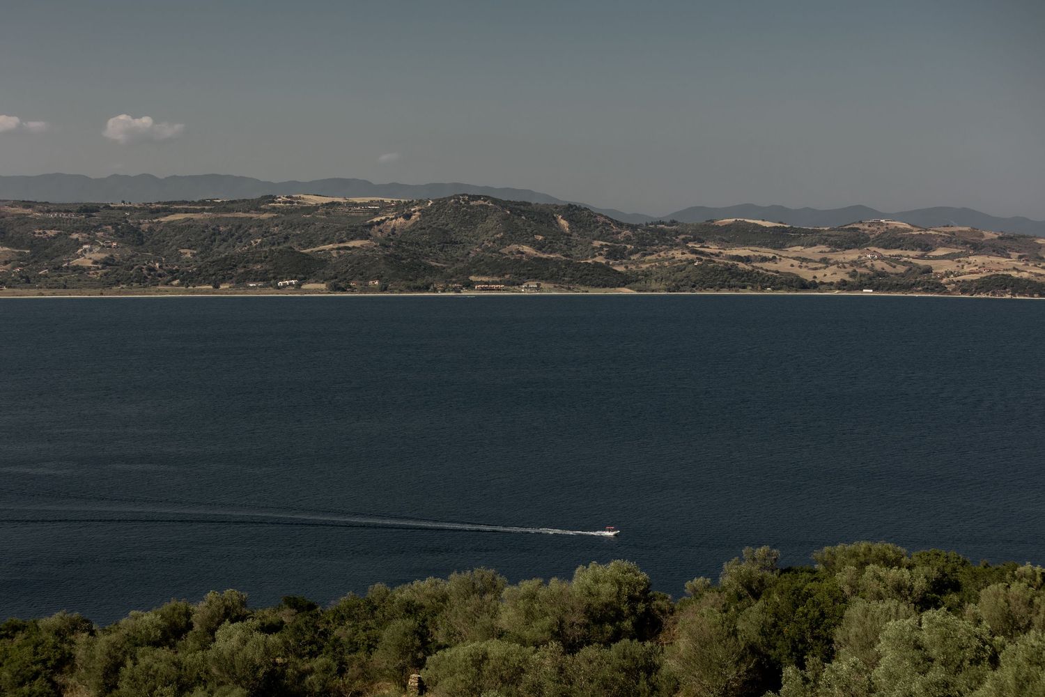 Scenic coastal landscape with mountains and blue water, small boat visible in distance.