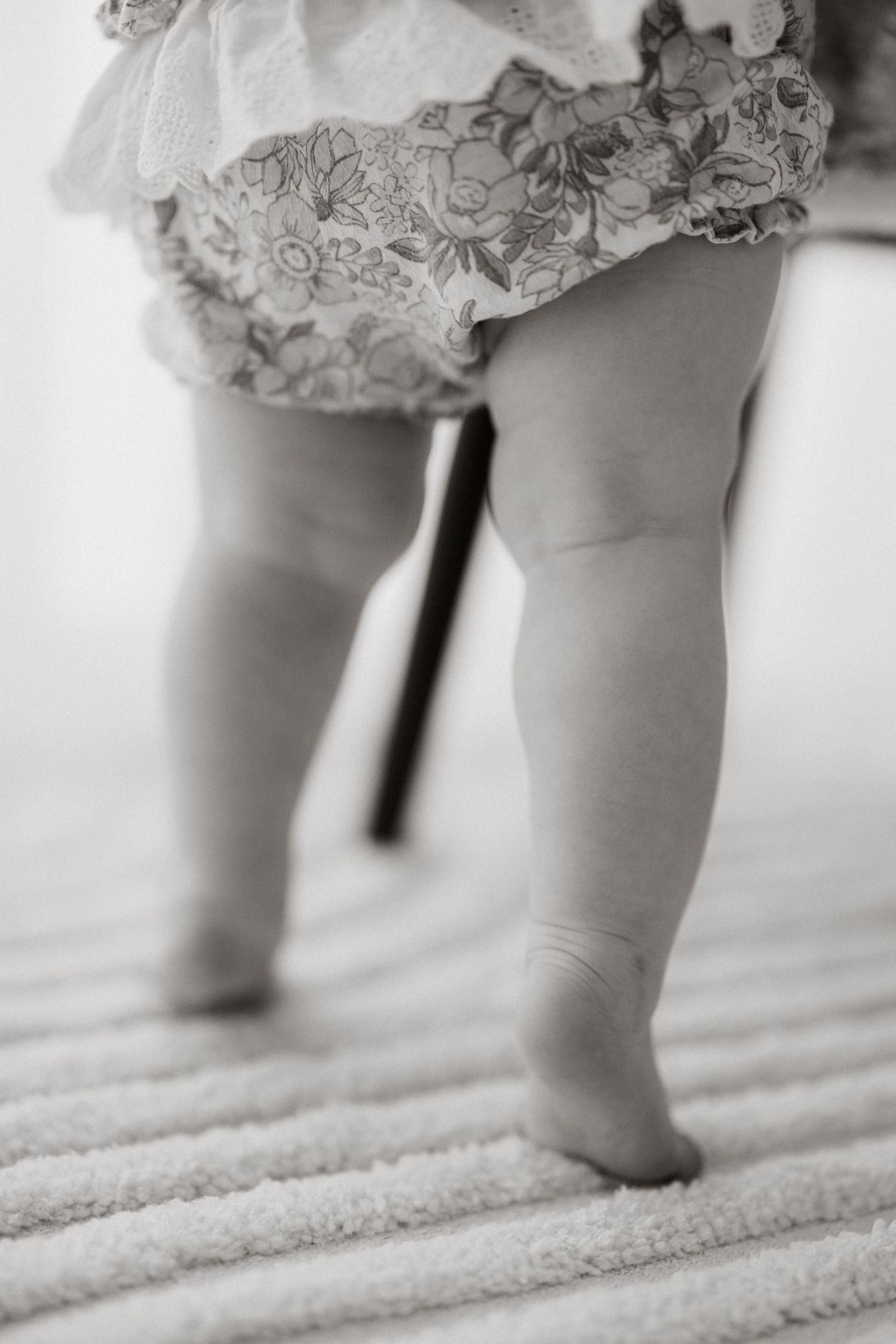 Close-up of tiny feet in delicate lace dress against white carpet.