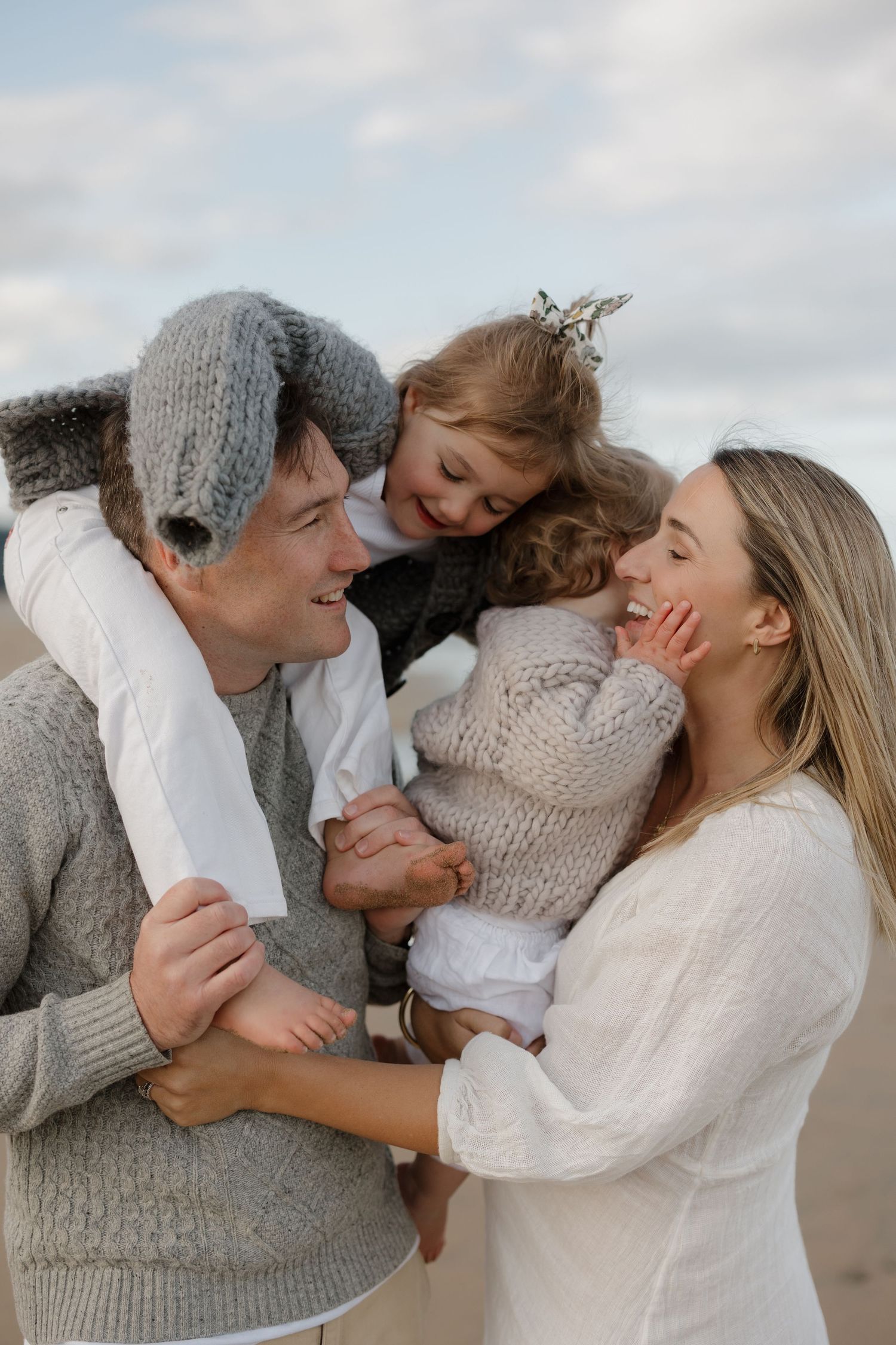 Intimate family moments shared on cloudy beach wearing coordinated cream and gray outfits.