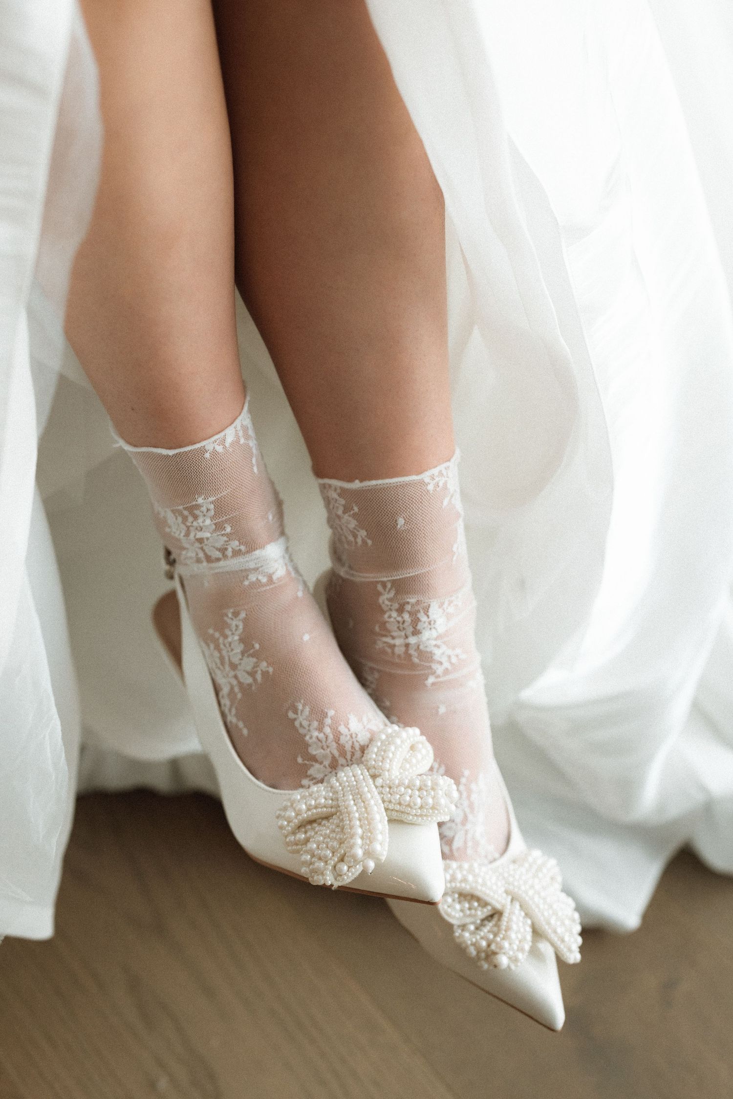 Delicate lace bridal shoes with embellished bows against flowing white fabric.