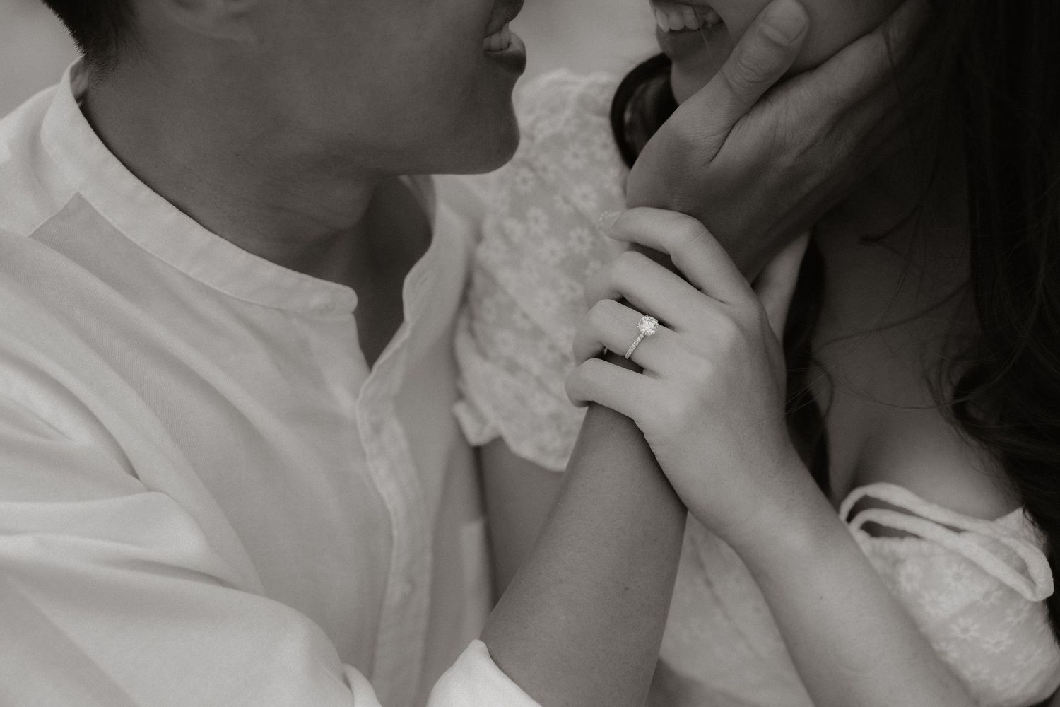 An intimate black and white close-up of hands touching in romantic embrace.