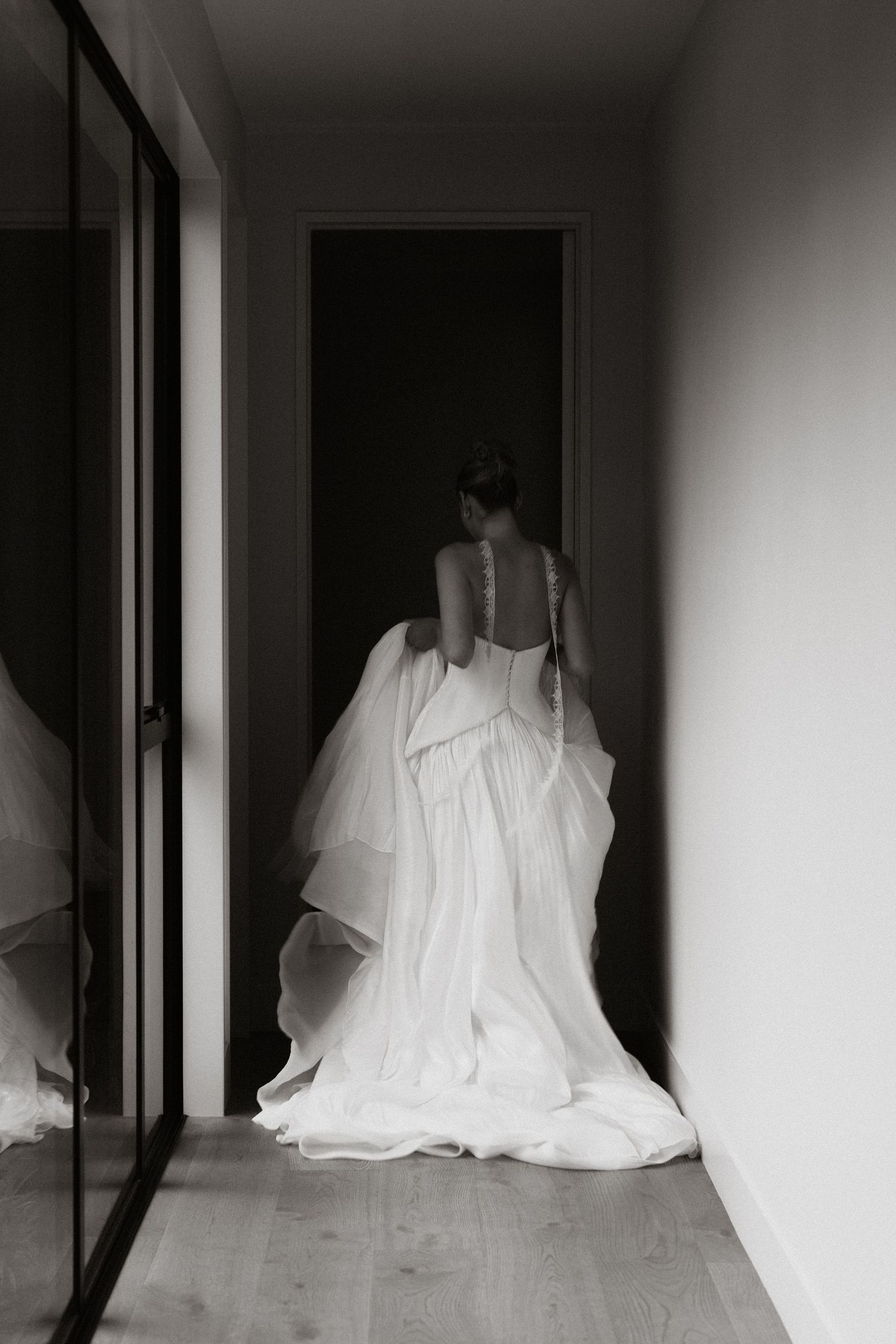 Dramatic silhouettes of wedding dress trailing through minimalist white hallway.