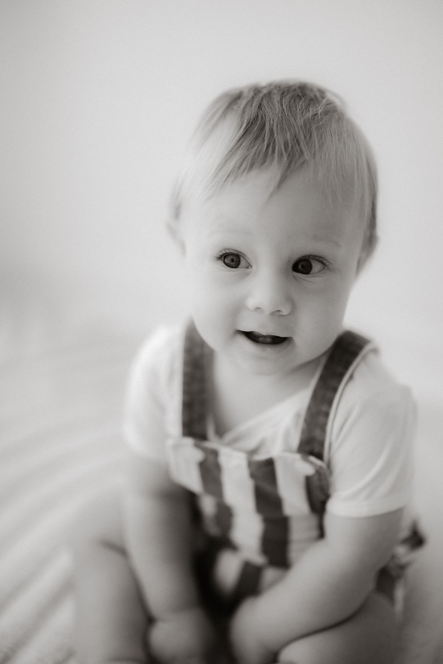 Black and white portrait of baby in striped overalls with gentle smile.