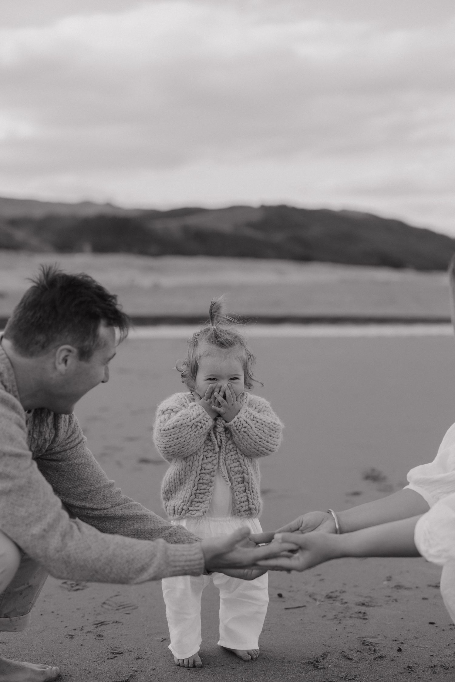 Black and white beach photo showing tender family interaction on sandy shore.