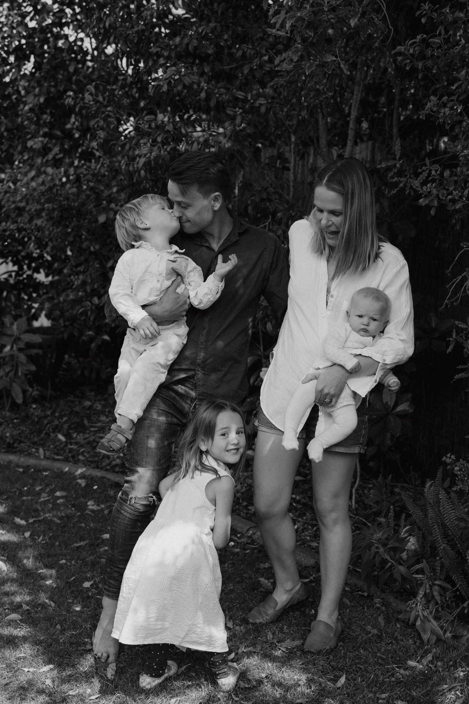 Playful family interactions captured in a series of black and white photos among garden foliage.