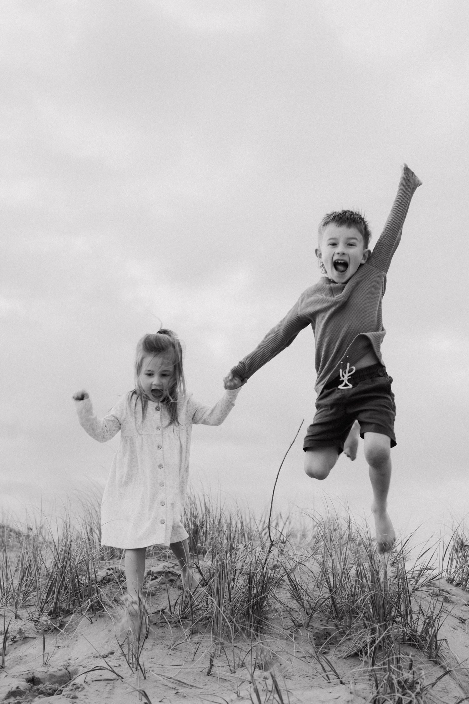 Energetic figures jumping and playing on sandy dunes against cloudy sky.