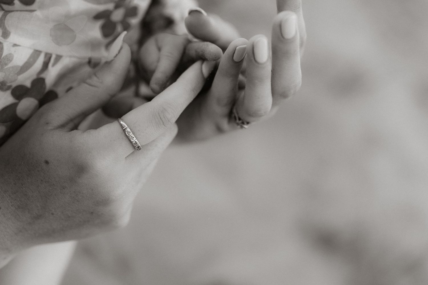 Black and white close-up photograph of hands holding while showing a wedding ring.