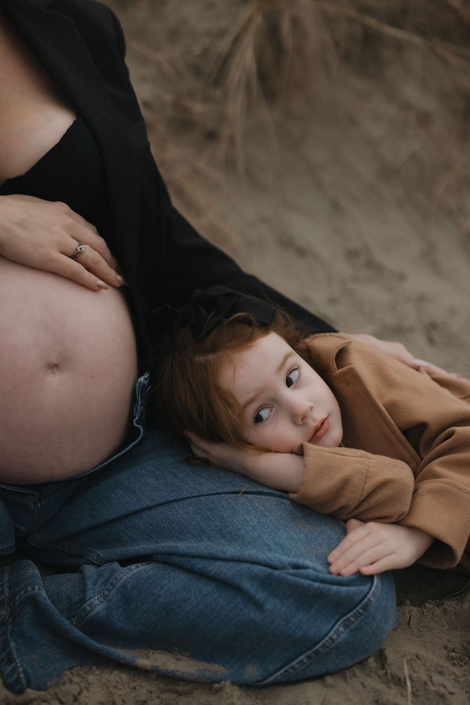 A tender maternity moment captured in moody lighting against natural backdrop.