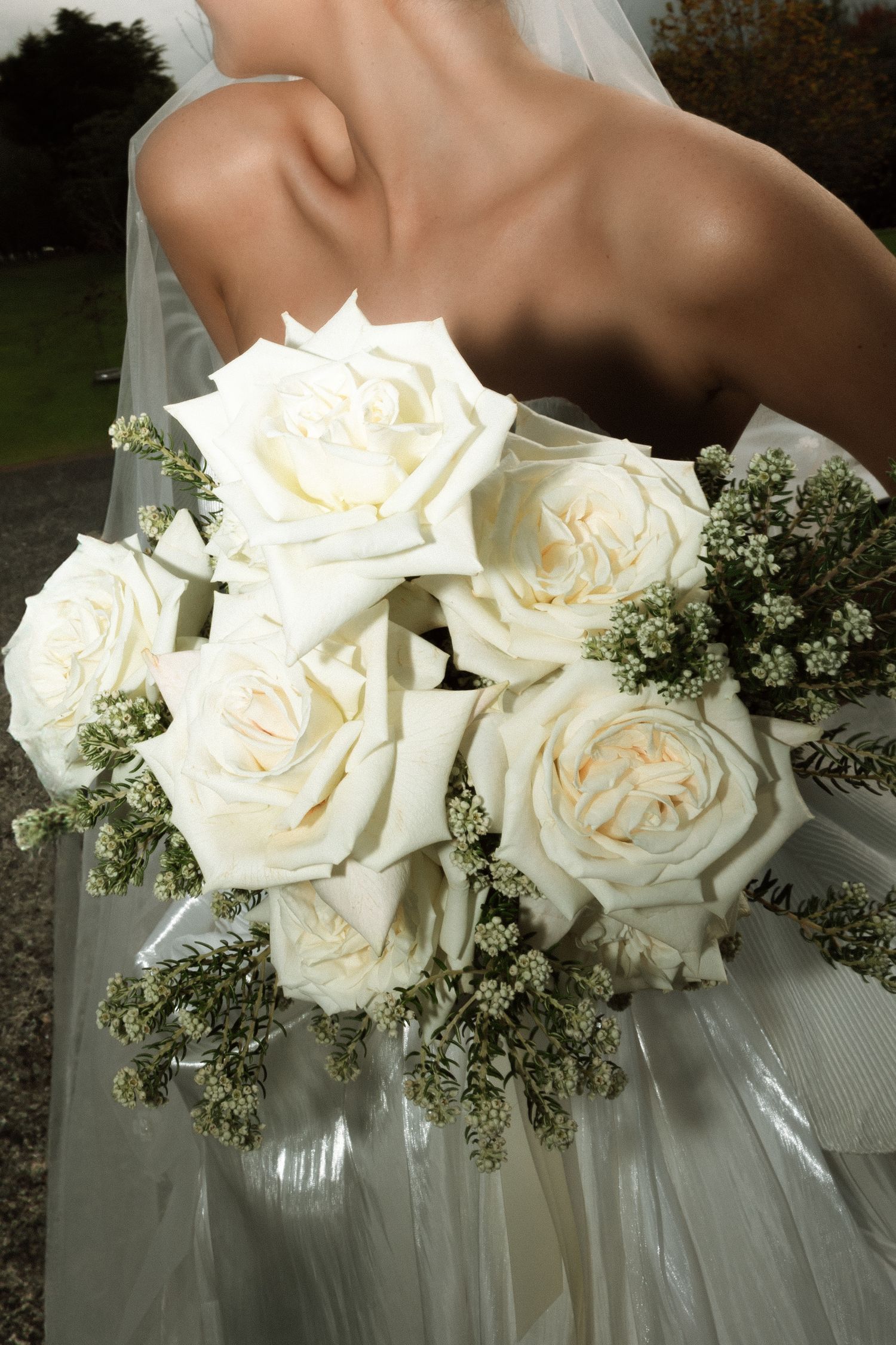 Elegant white rose bridal bouquet with baby's breath against a wedding dress.