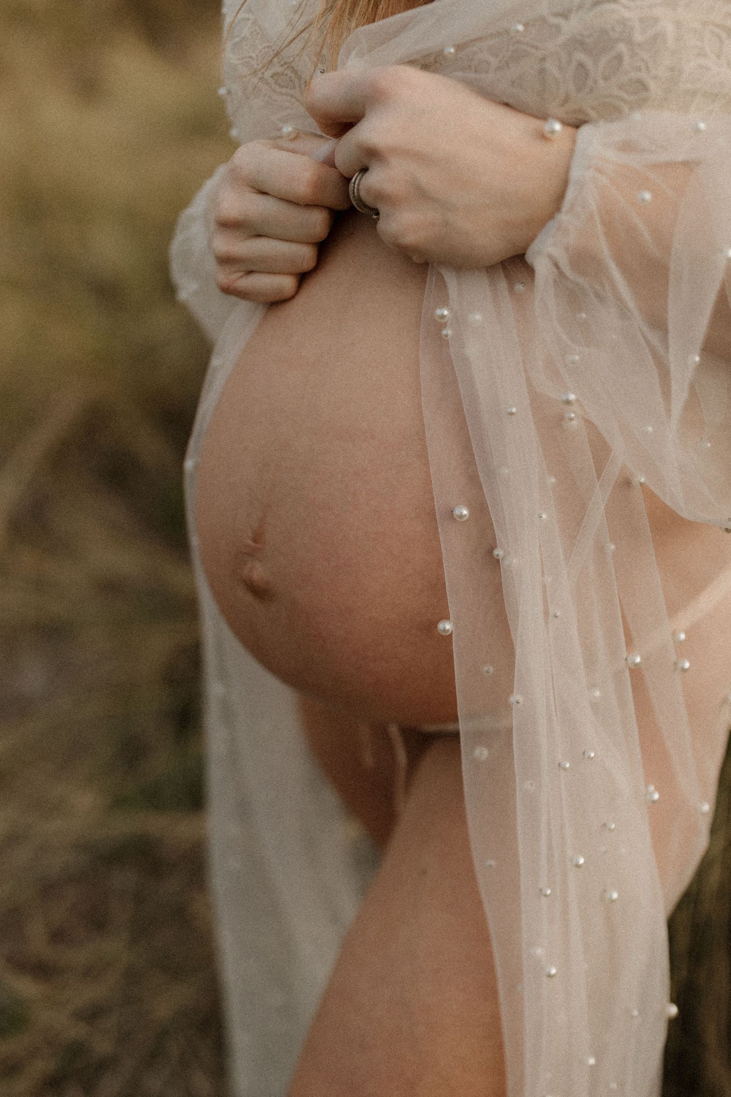 Close-up of pregnant belly draped in delicate sheer fabric with sparkling details.