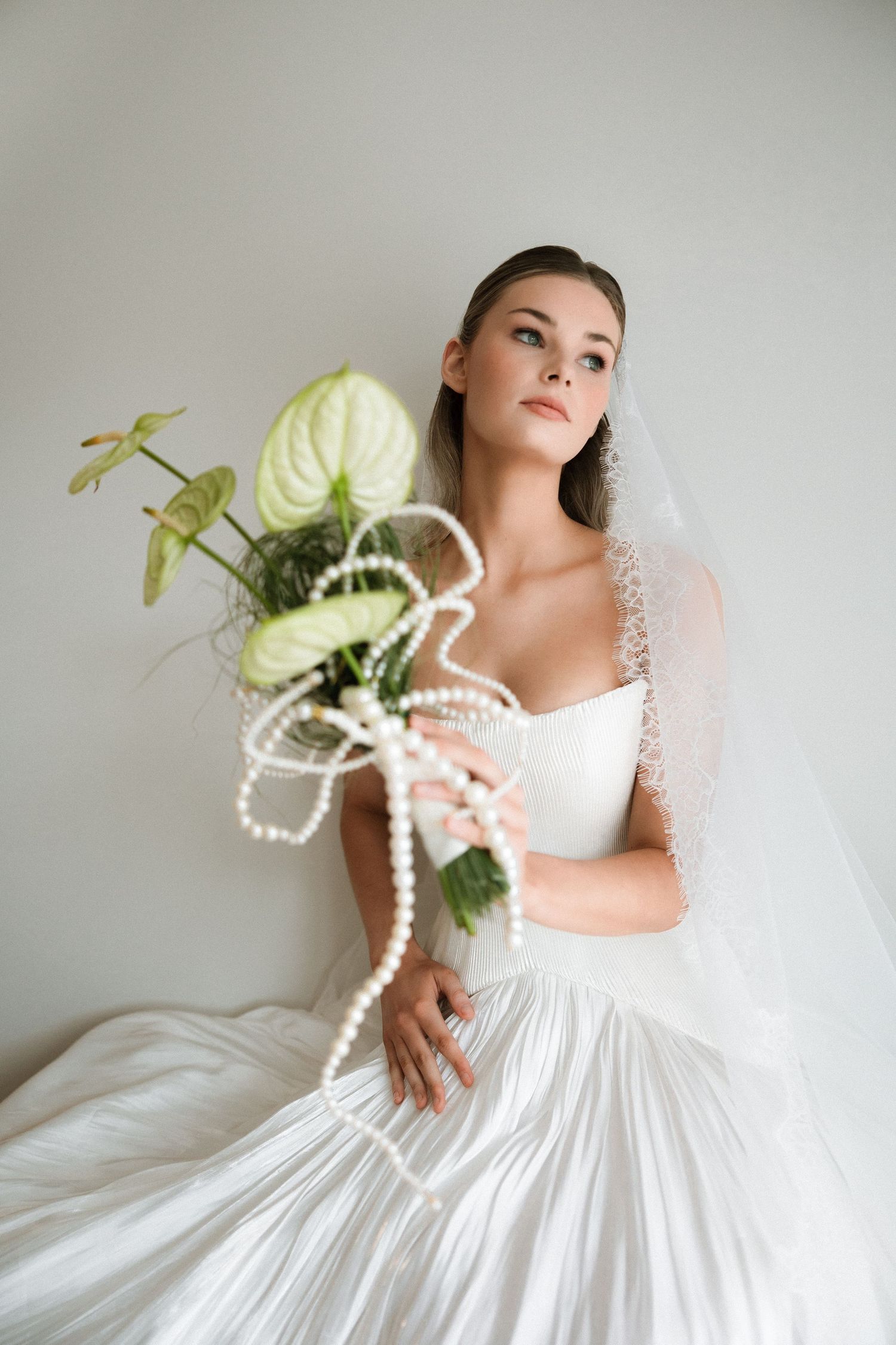 Elegant bridal portraits showcase a white dress with pearl accessories and green floral accents.