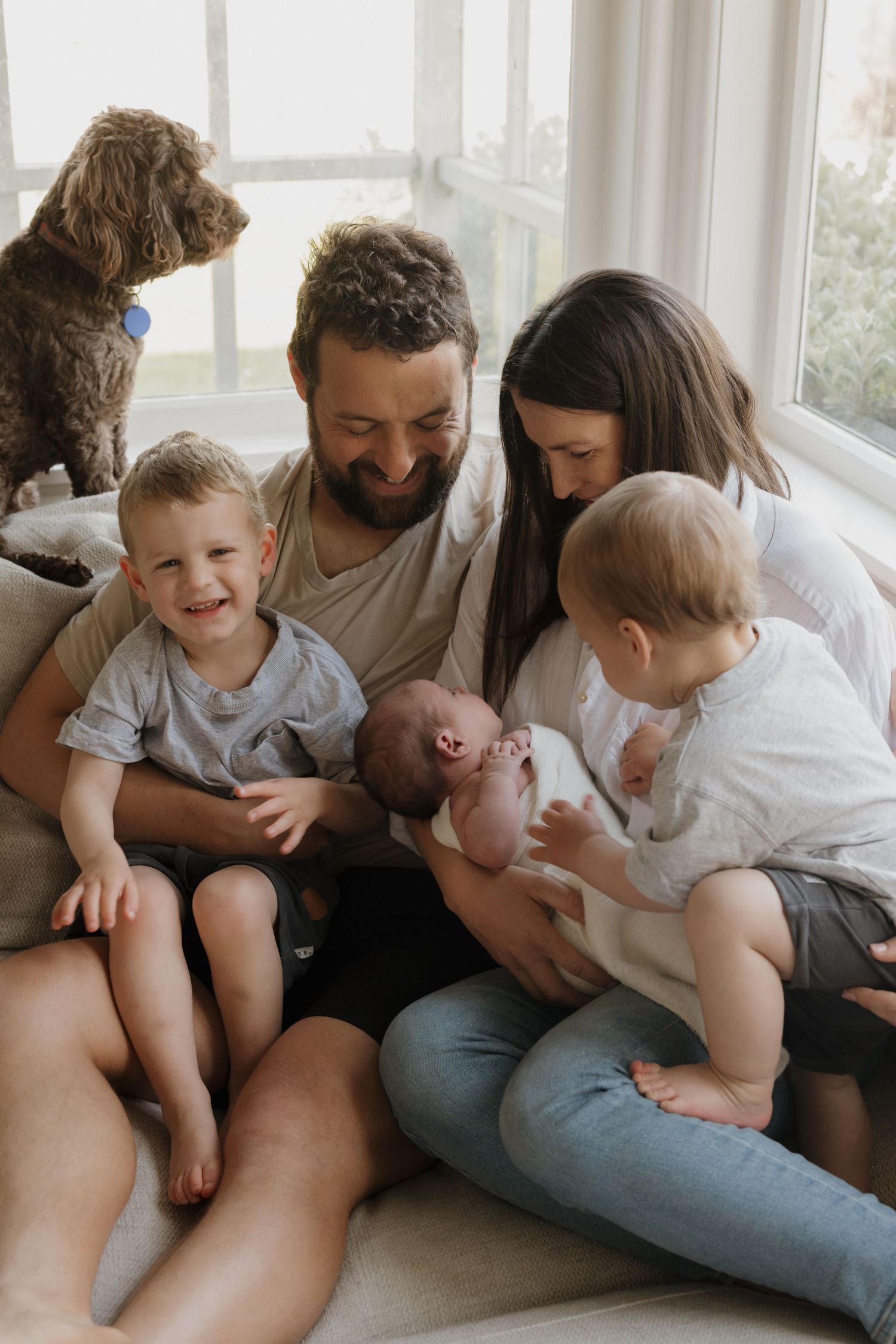 Happy family with dog gathered on windowsill sharing intimate moment with newborn baby.