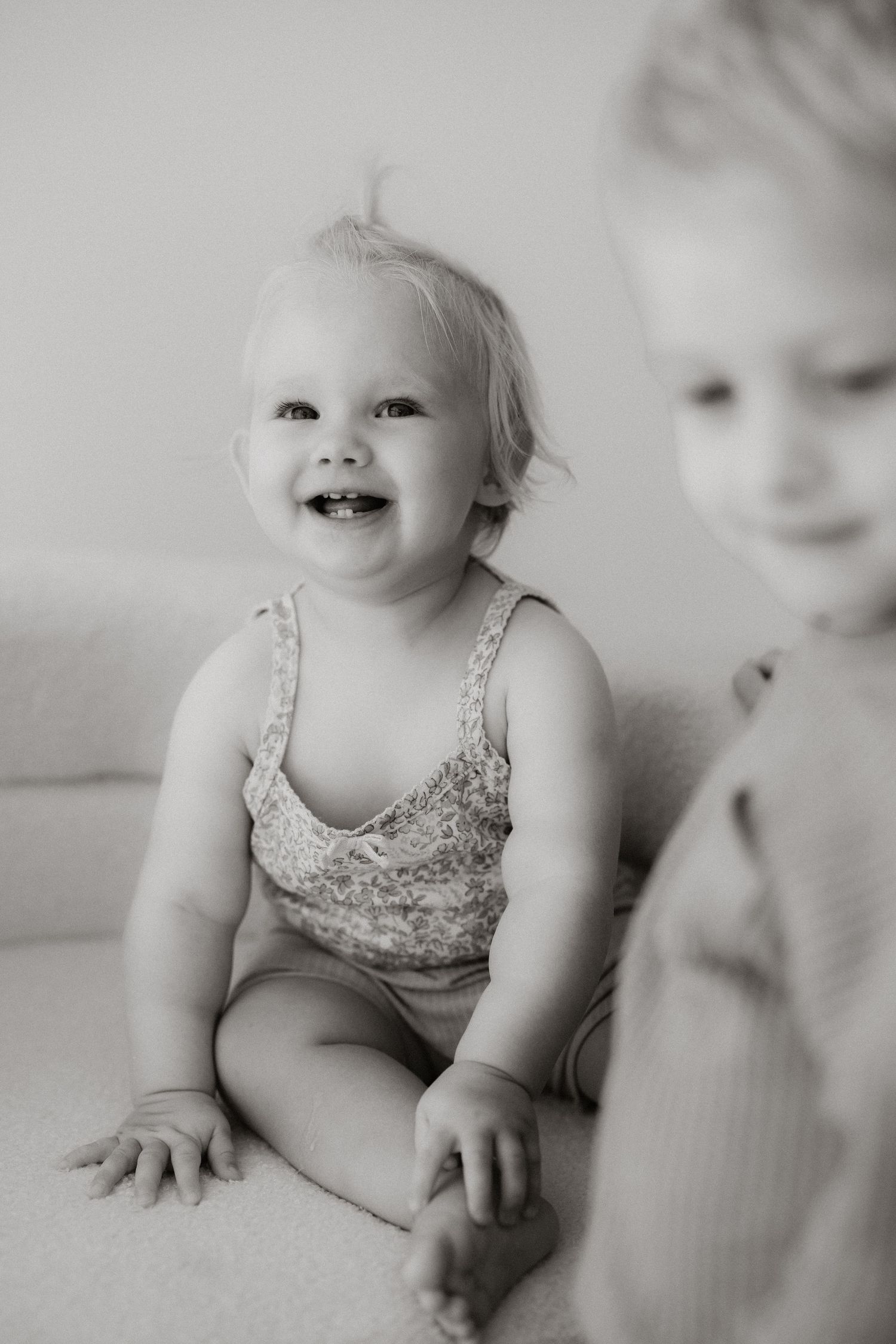 Black and white artistic photo series showing a baby in a floral dress sitting and playing in soft natural light.