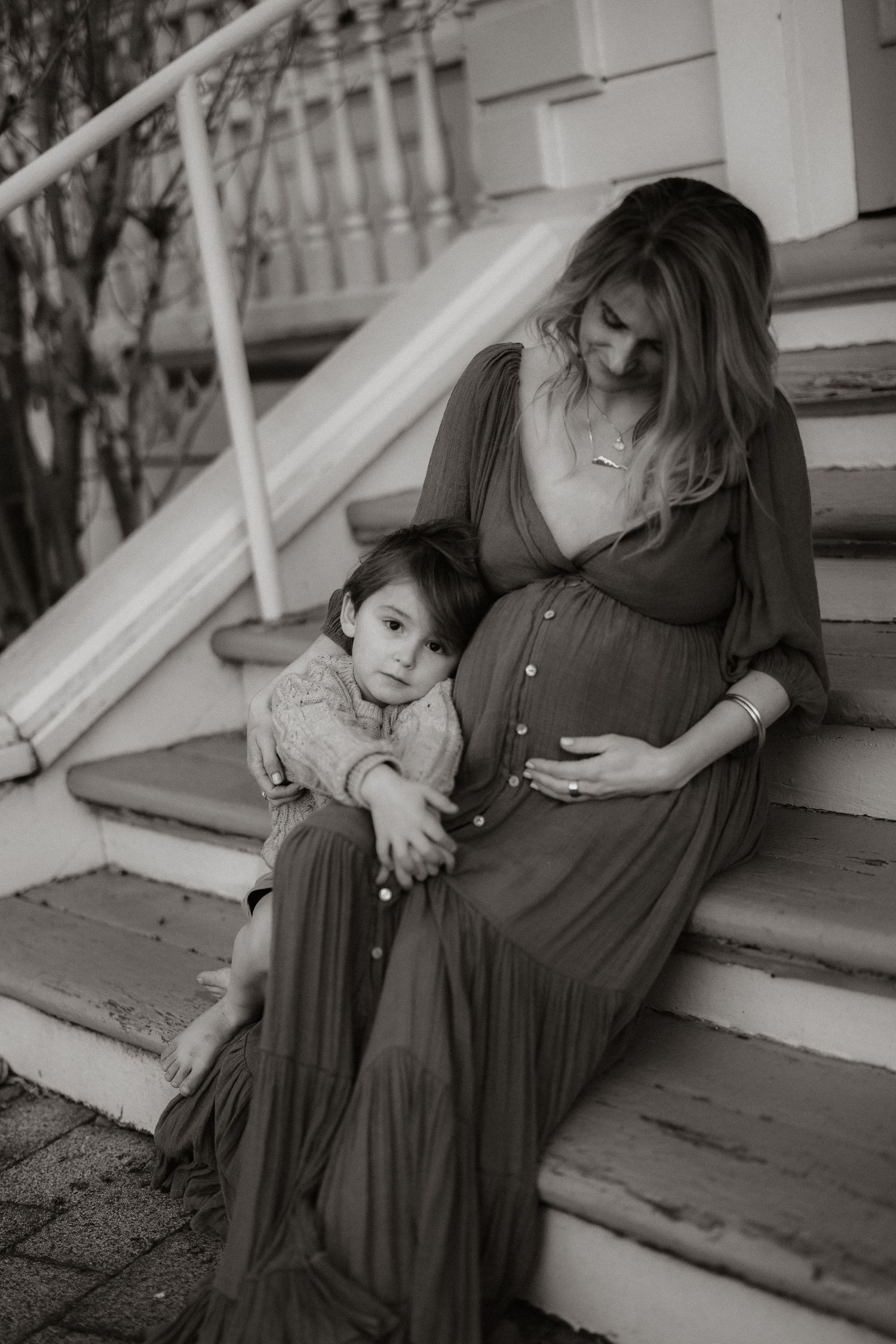 Black and white candid photo of a parent and child sharing intimate moments sitting on porch steps.