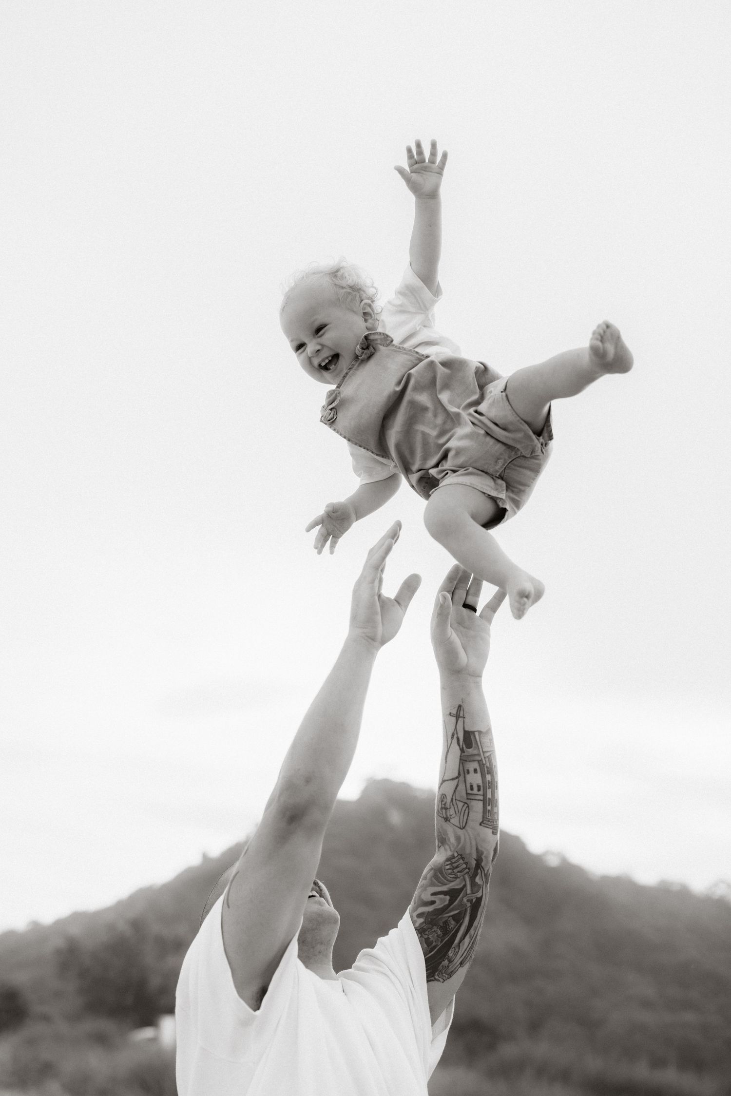 Parent lovingly tosses a happy baby in the air at sunset, creating a touching moment of joy and connection.