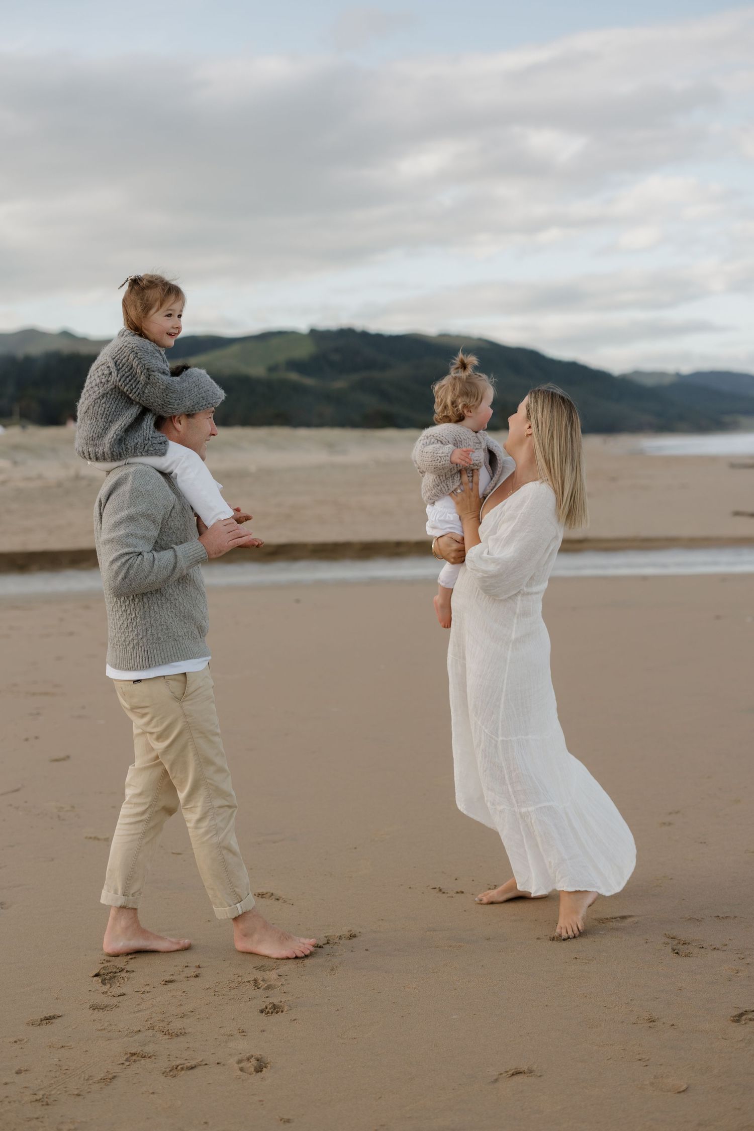 Family playing together on sandy beach with mountains in background.