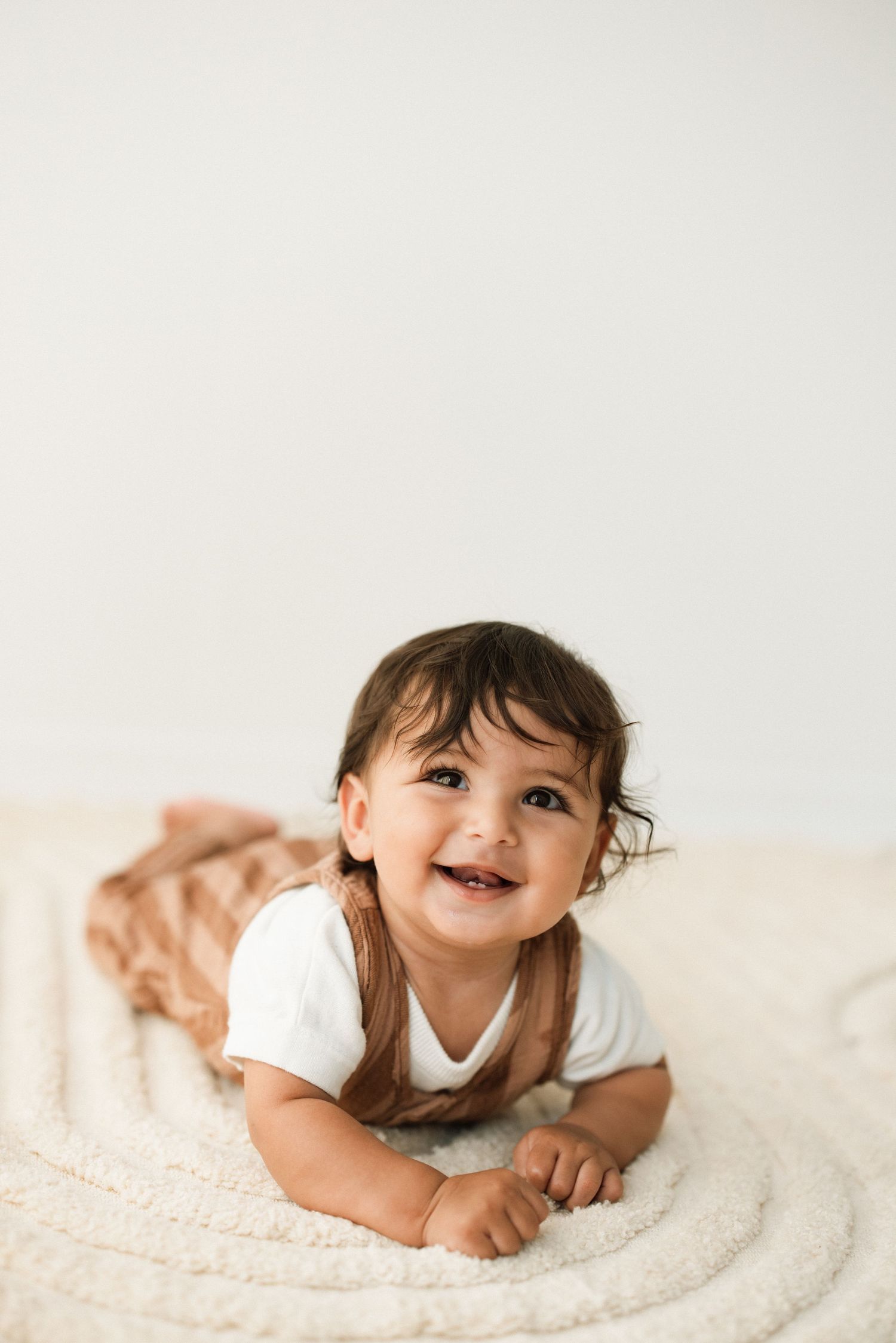 Happy baby crawling and smiling on cream textured blanket.