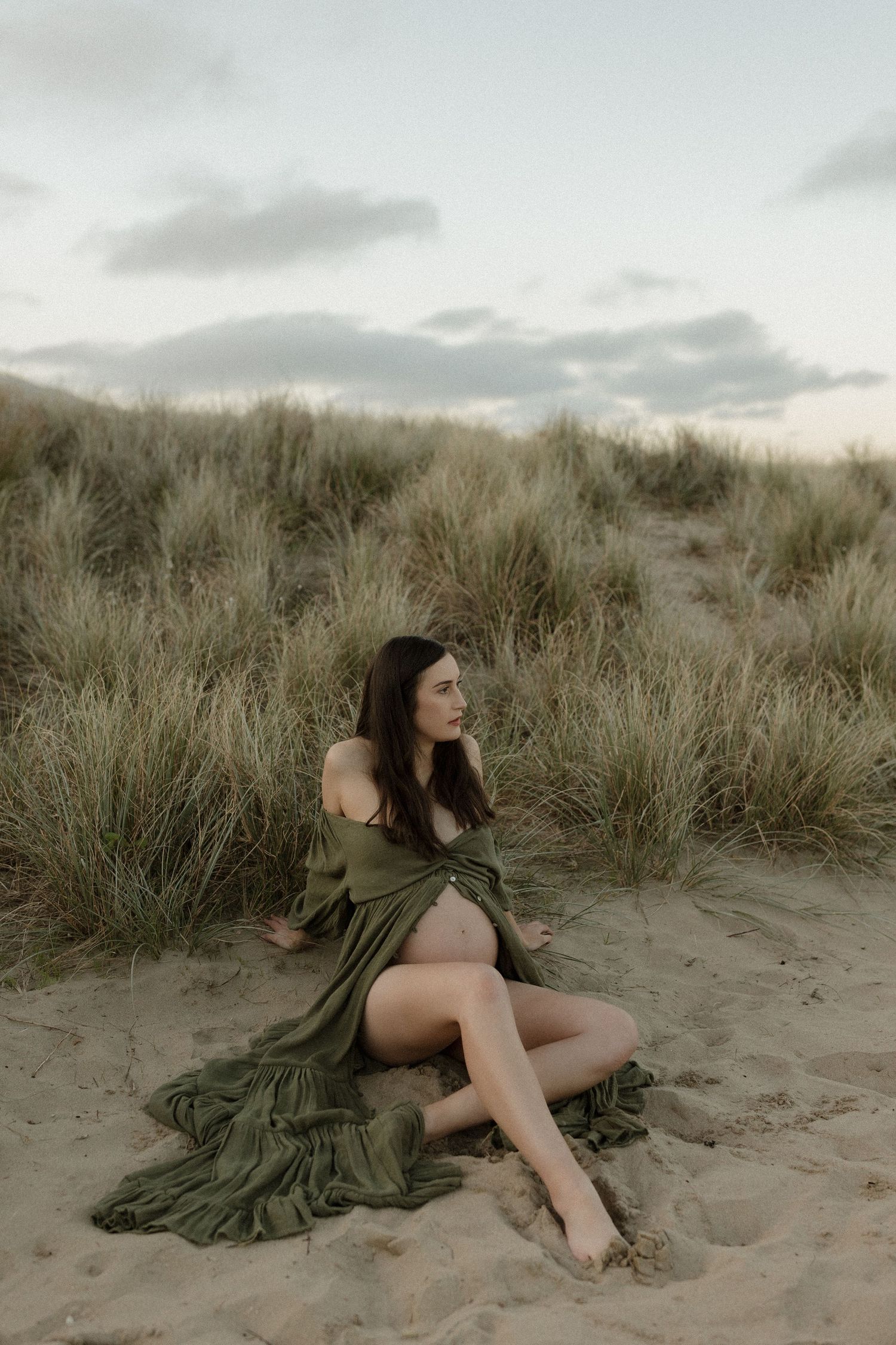 Woman in flowing green dress reclining on sandy dunes at twilight.