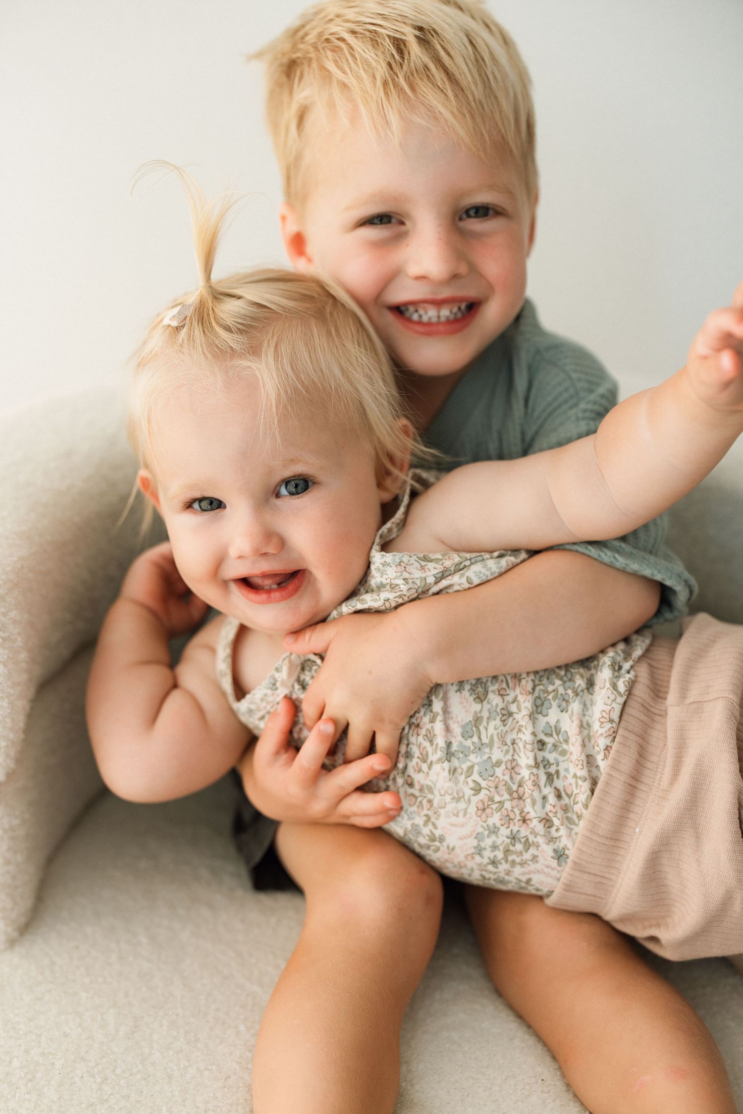 Two siblings sharing joyful laughter while cuddling on gray couch.