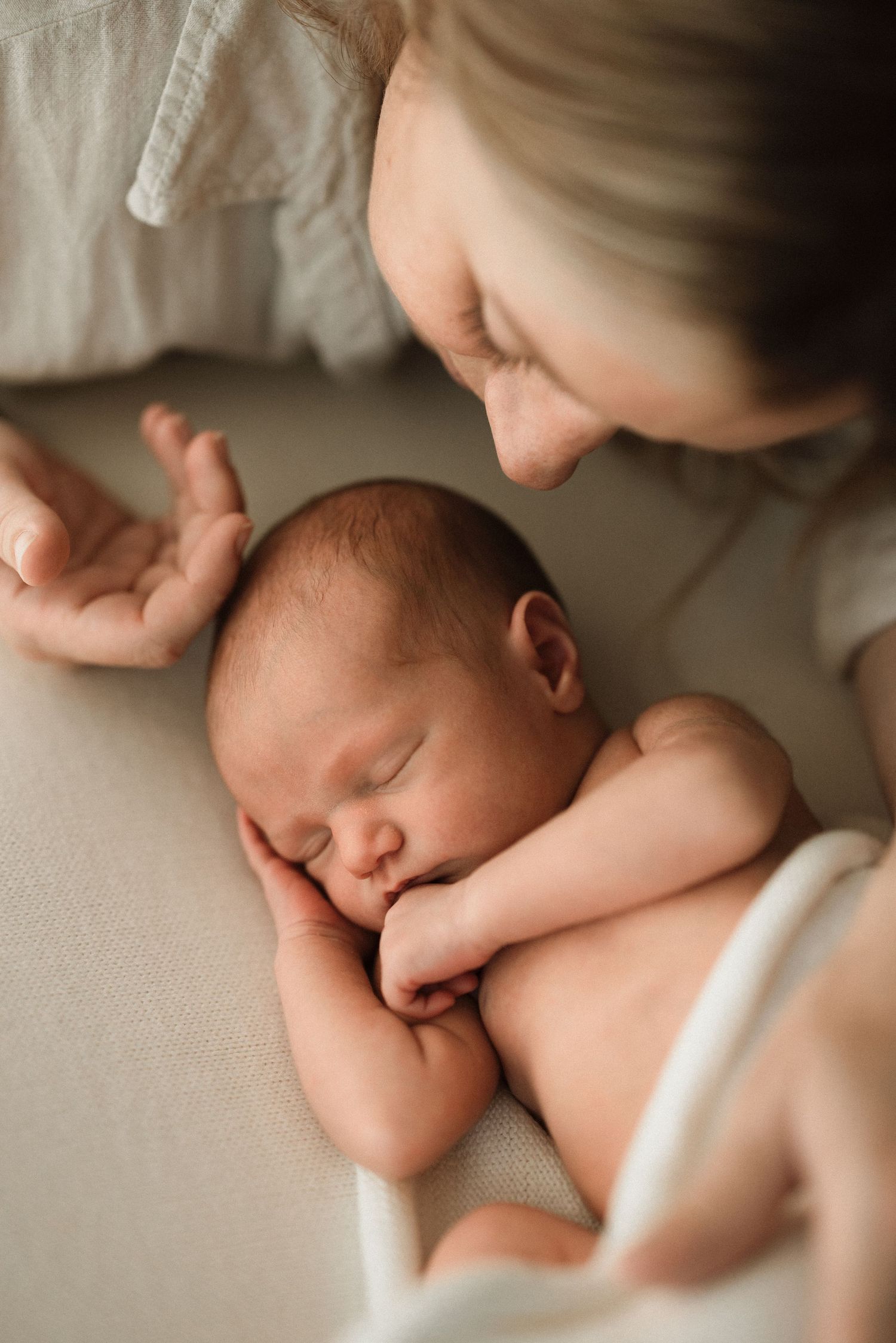 Tender moment captured between sleeping newborn and caregiver in warm natural light.