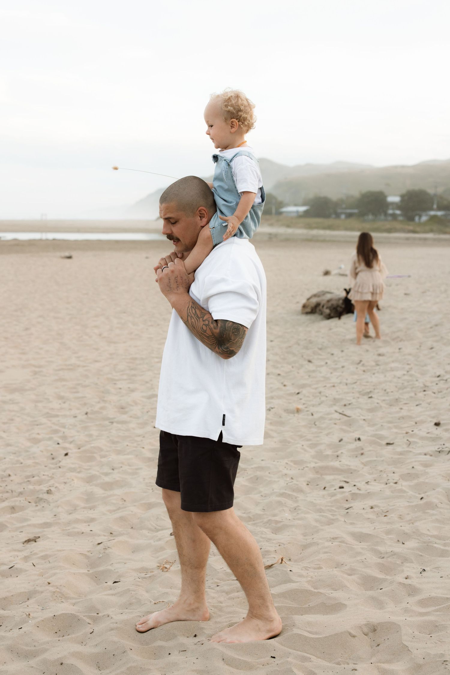 A heartwarming scene at the beach shows a caring adult carrying a child while walking along the sandy shore.