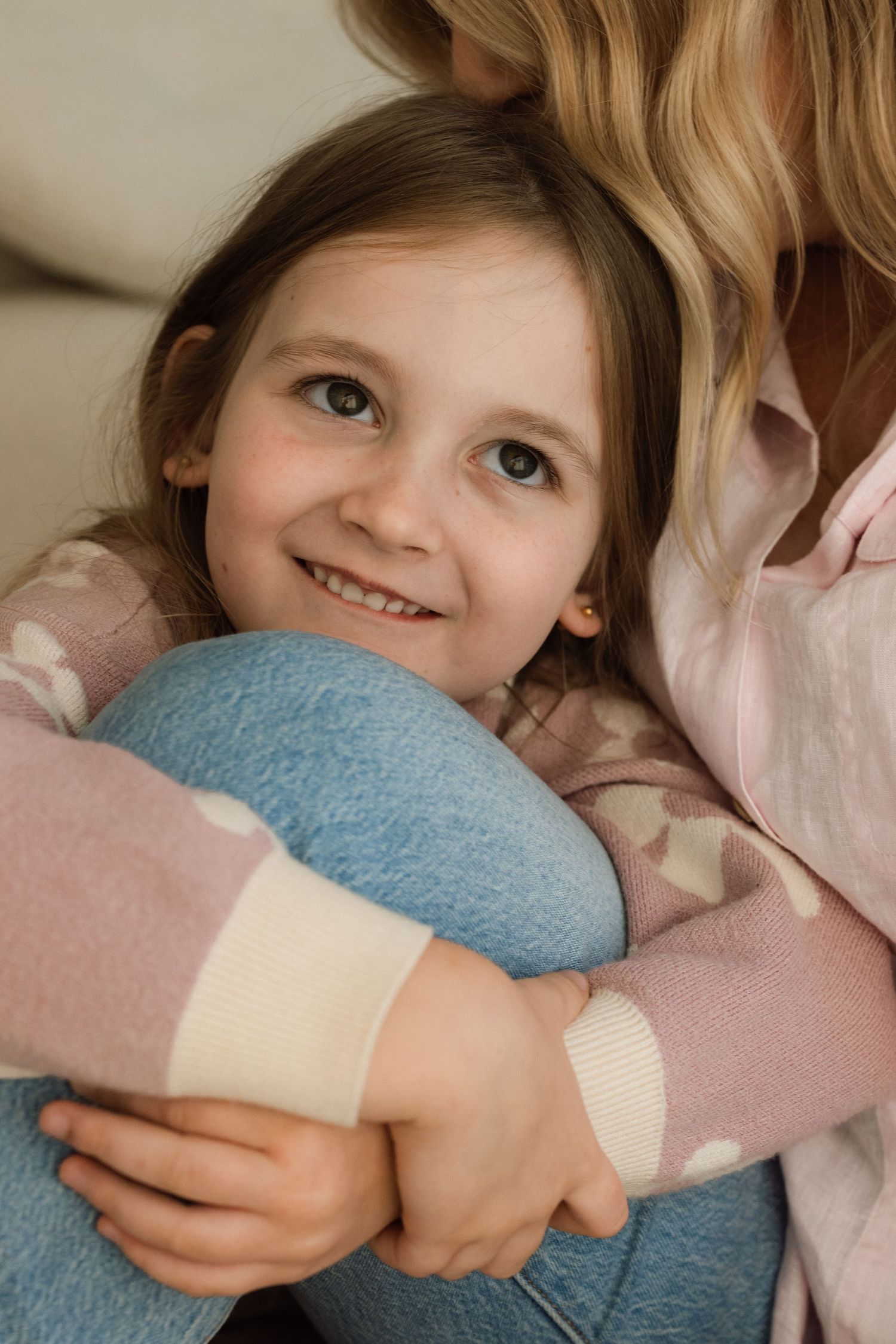 A young child lies on pink bedding while hugging a soft blue pillow or cushion.