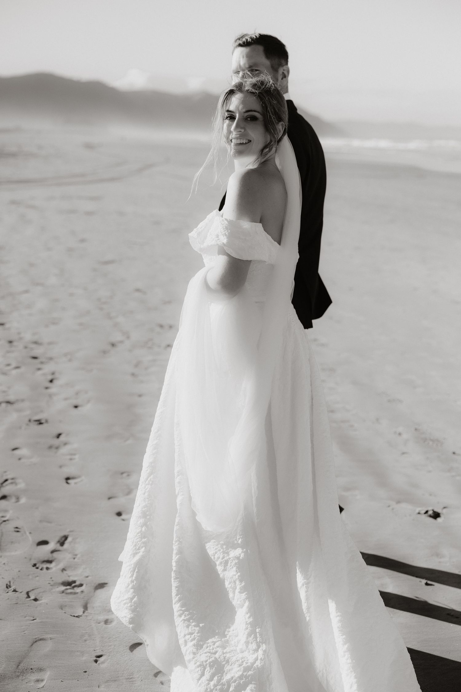 A black and white beach wedding portrait showing couple in formal attire on sandy shore.