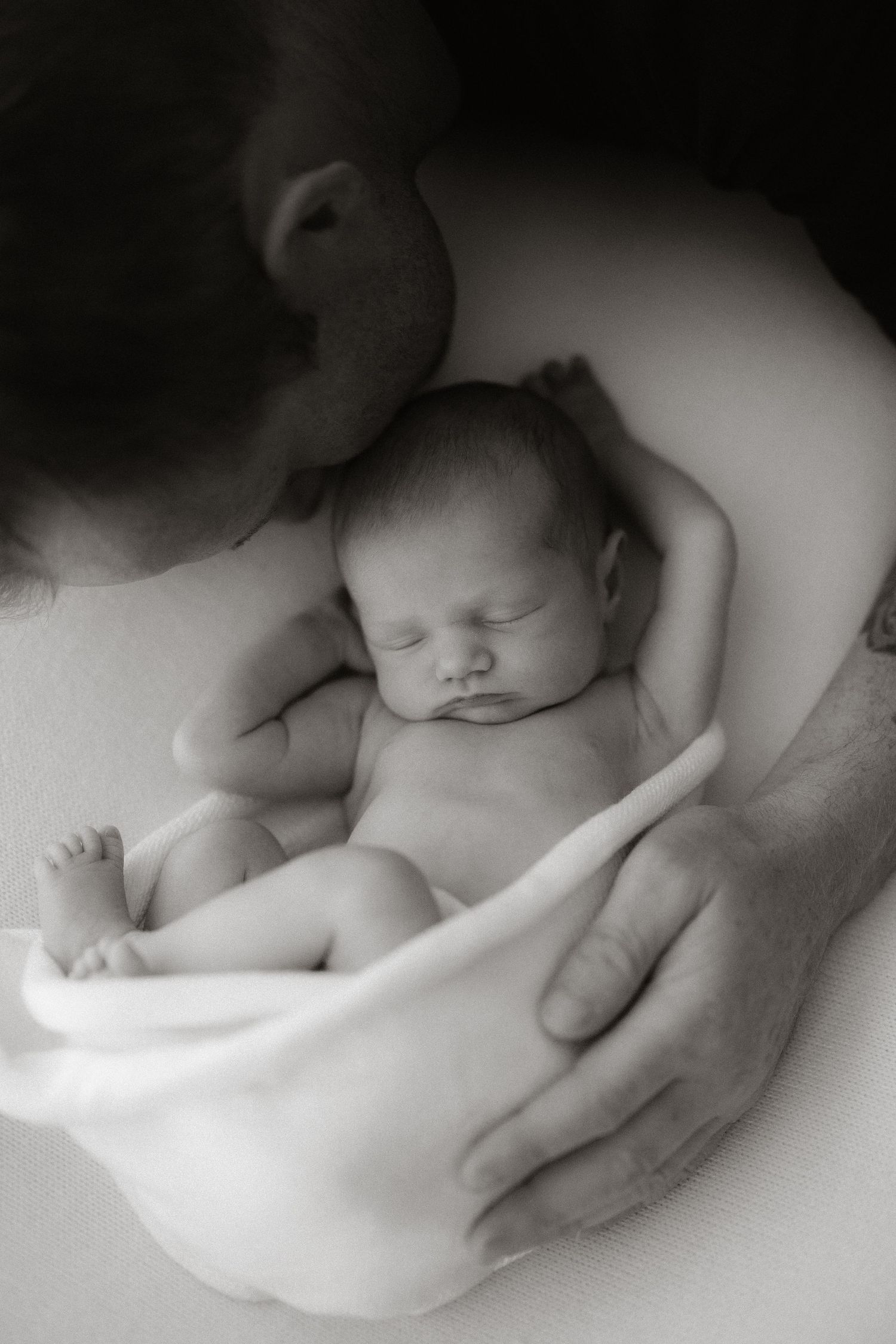 Intimate black and white portrait of sleeping newborn being cradled in gentle hands.