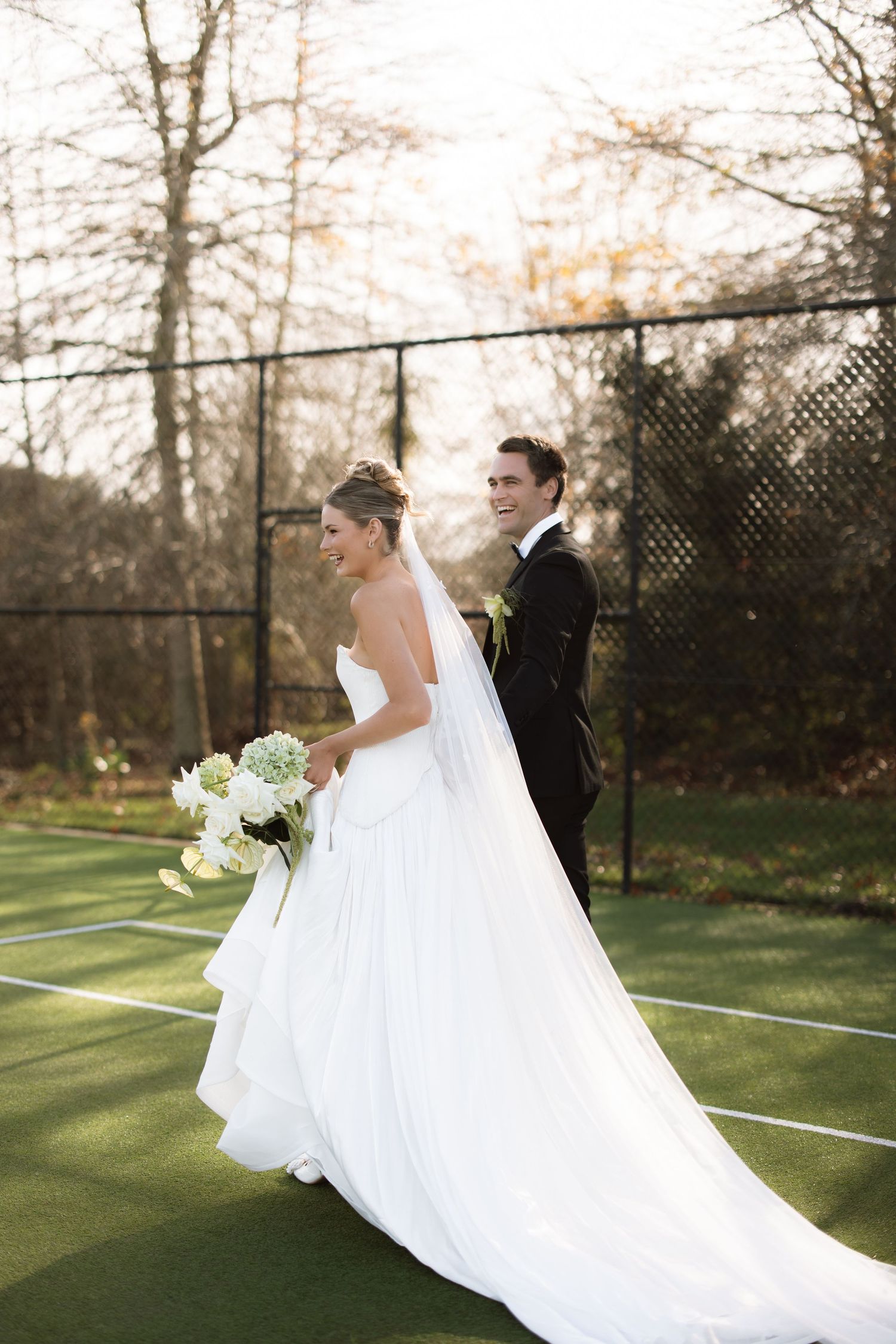 Romantic wedding photos on tennis court with flowing dress and autumn backdrop.