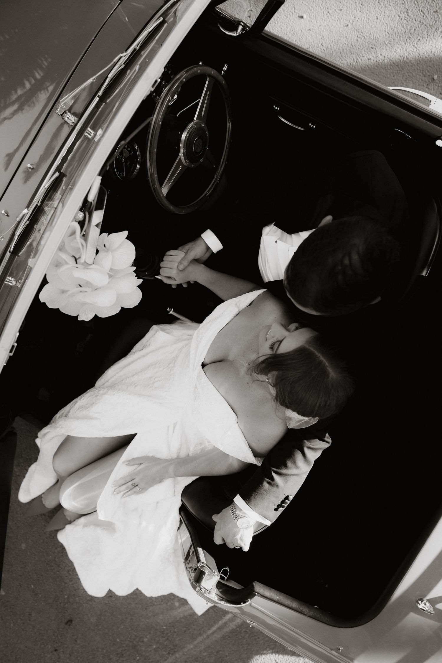 Wedding couple share a romantic moment in a car wearing formal attire.