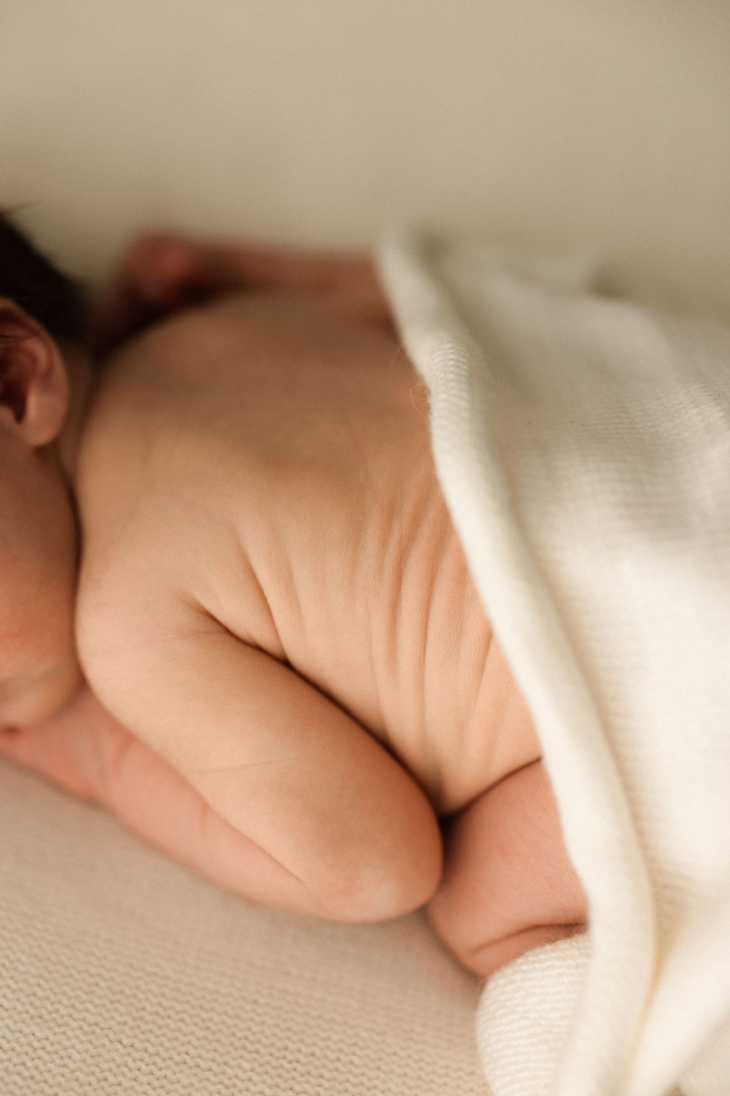 Close-up of a sleeping newborn baby's chubby legs and bottom covered with a soft white knit blanket.