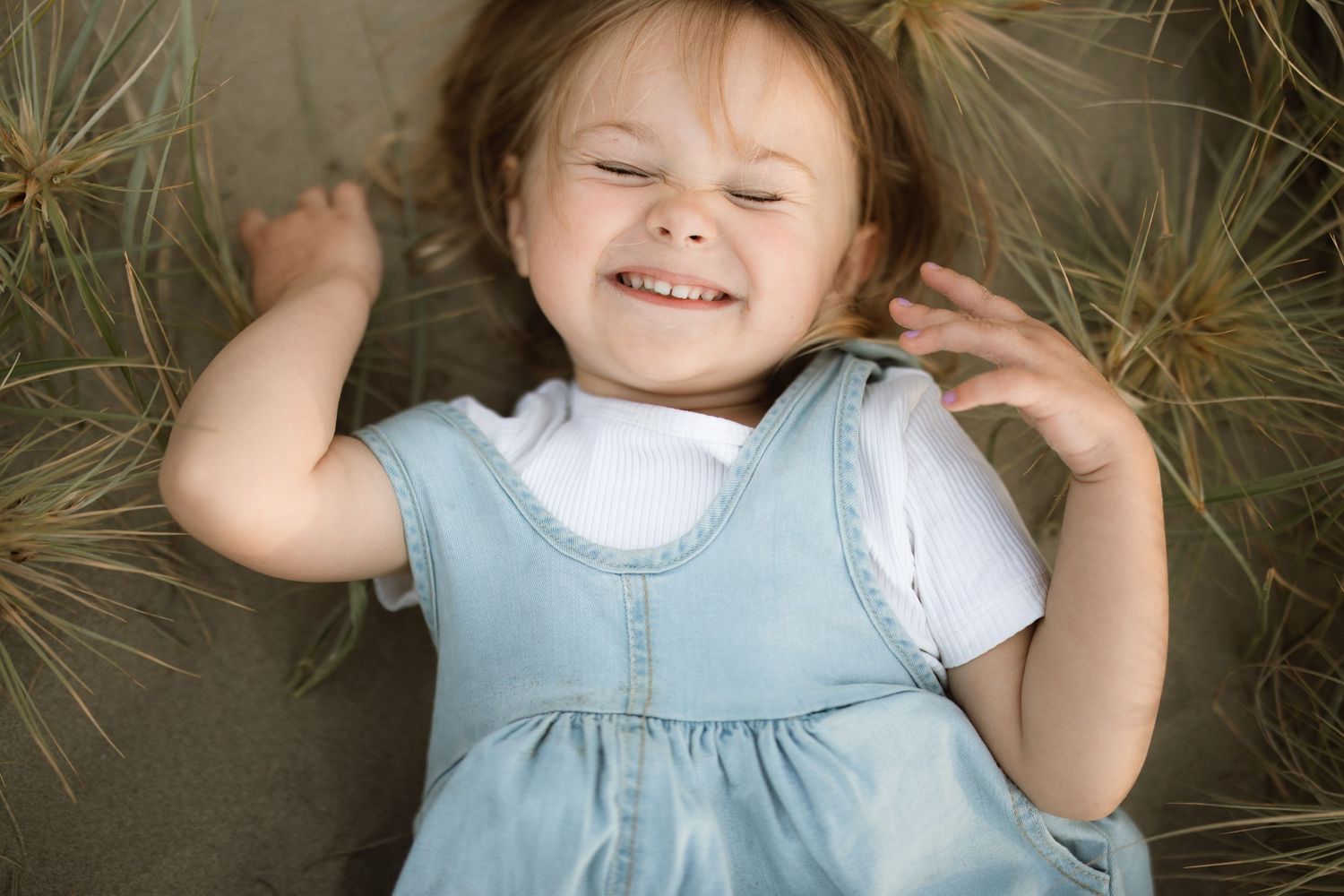 Multiple connected photos show a small child wearing a light blue dress lying in golden grass during an outdoor photo session.