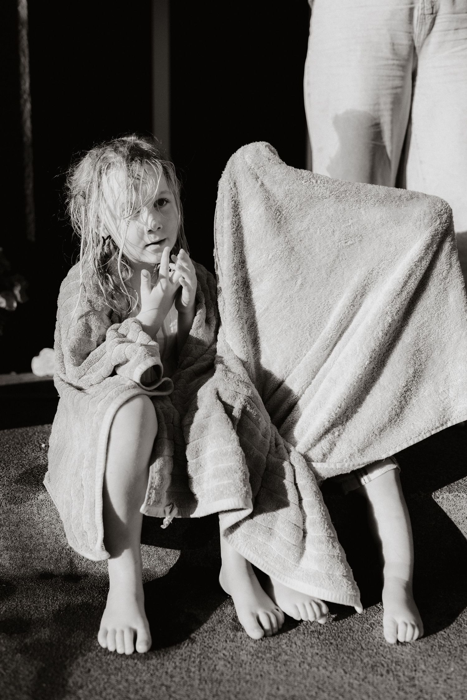 Black and white photo of a young girl in a robe crouching beside an adult wrapped in a towel.