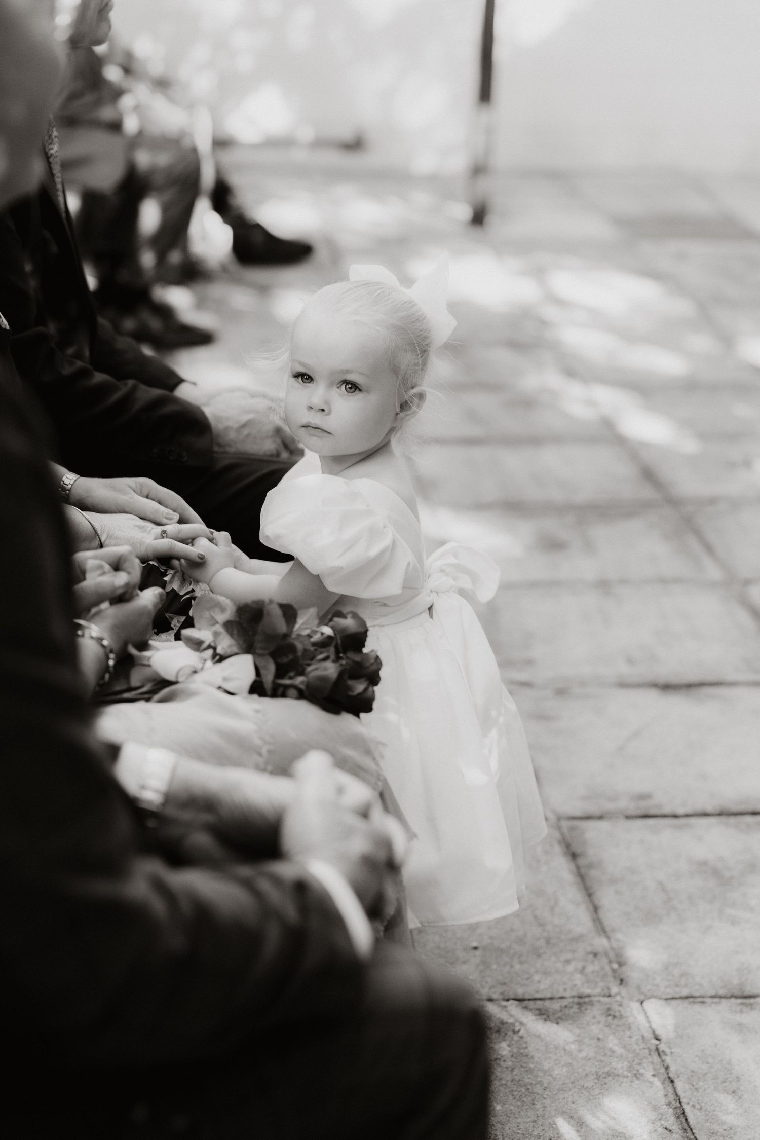 Small child in white dress reaches out during formal gathering.
