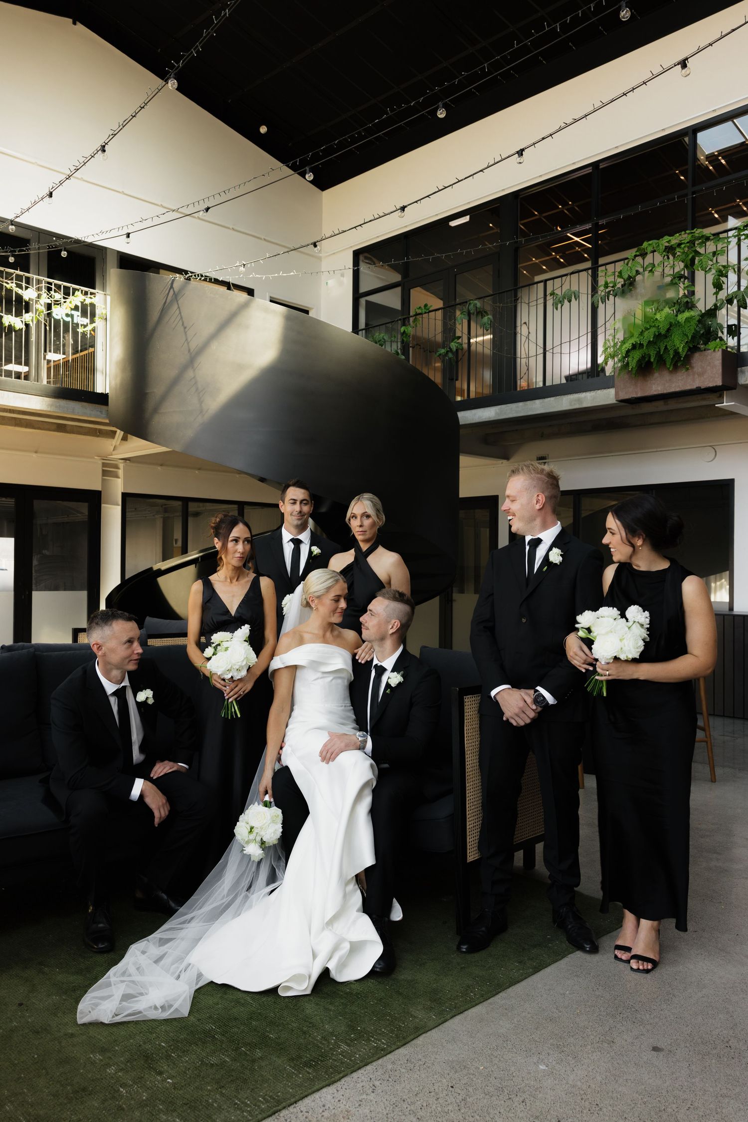 Wedding party in formal attire posed together in modern architectural setting.