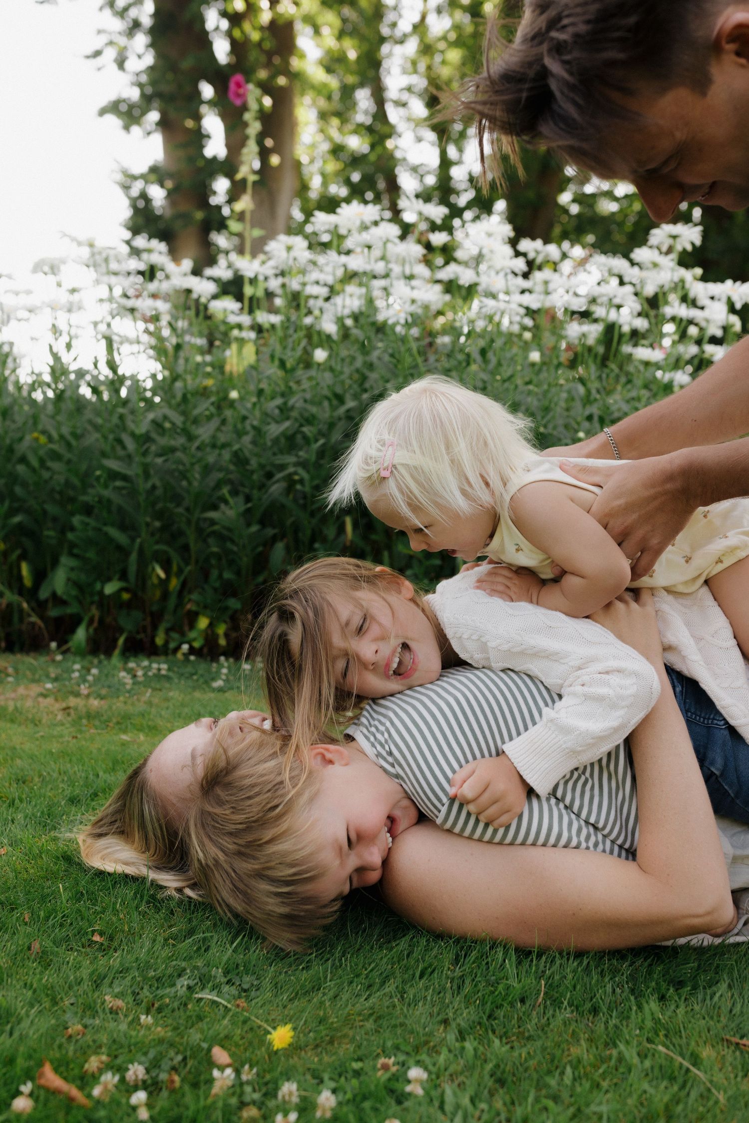 Children playing and laughing together on green grass in a garden with white flowers blooming in the background.