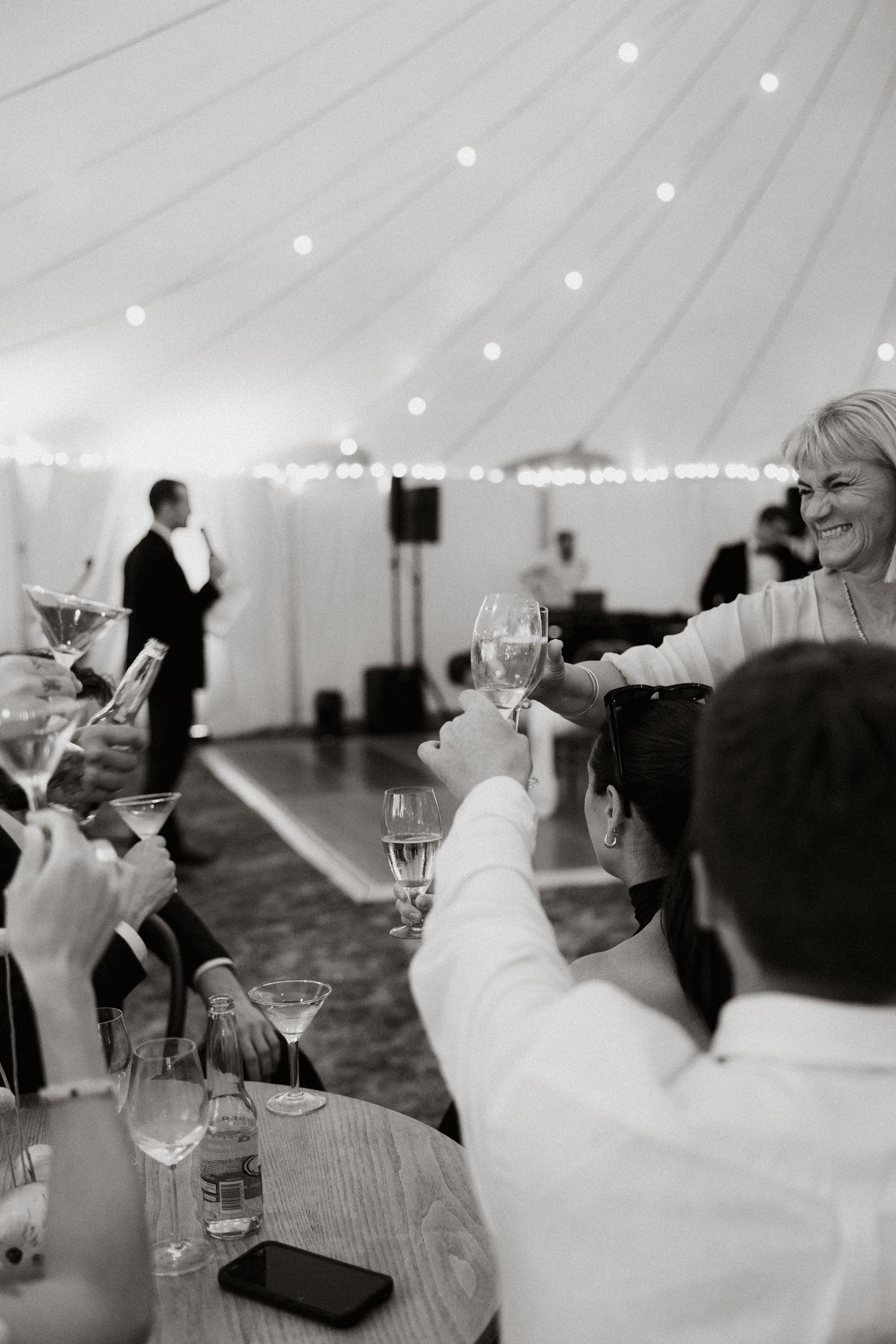 Black and white reception scene inside elegant white tent with guests raising glasses.