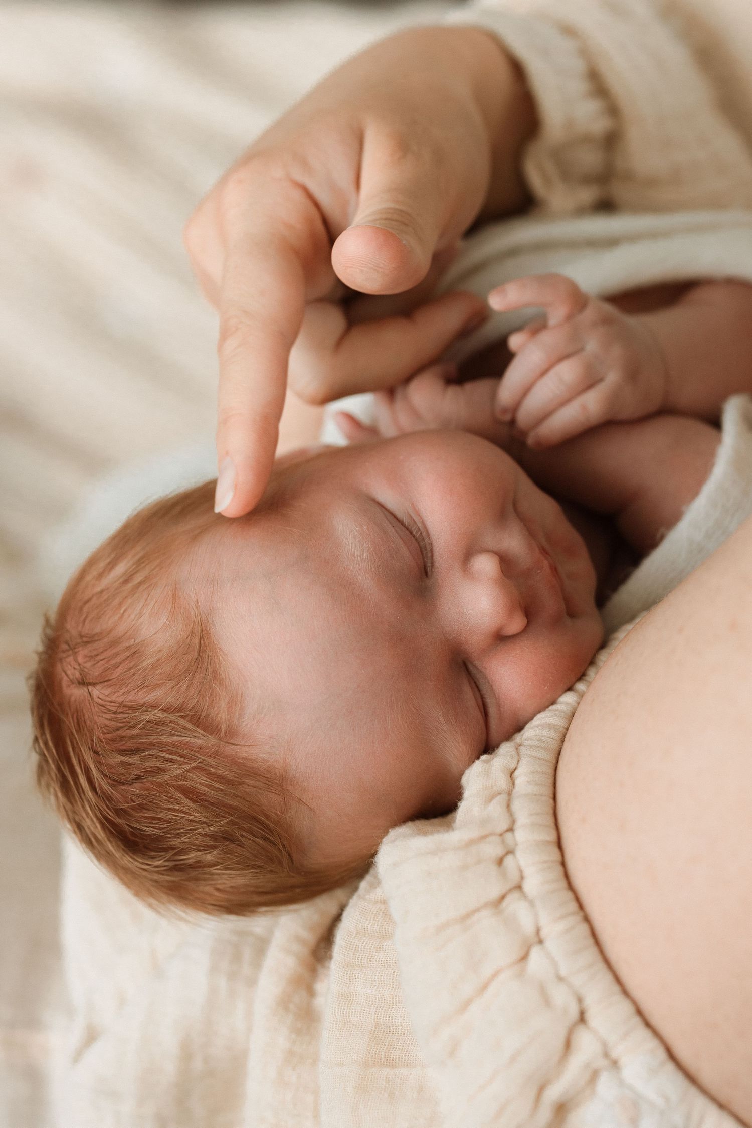 Gentle hand touching sleeping baby's face in soft natural light.