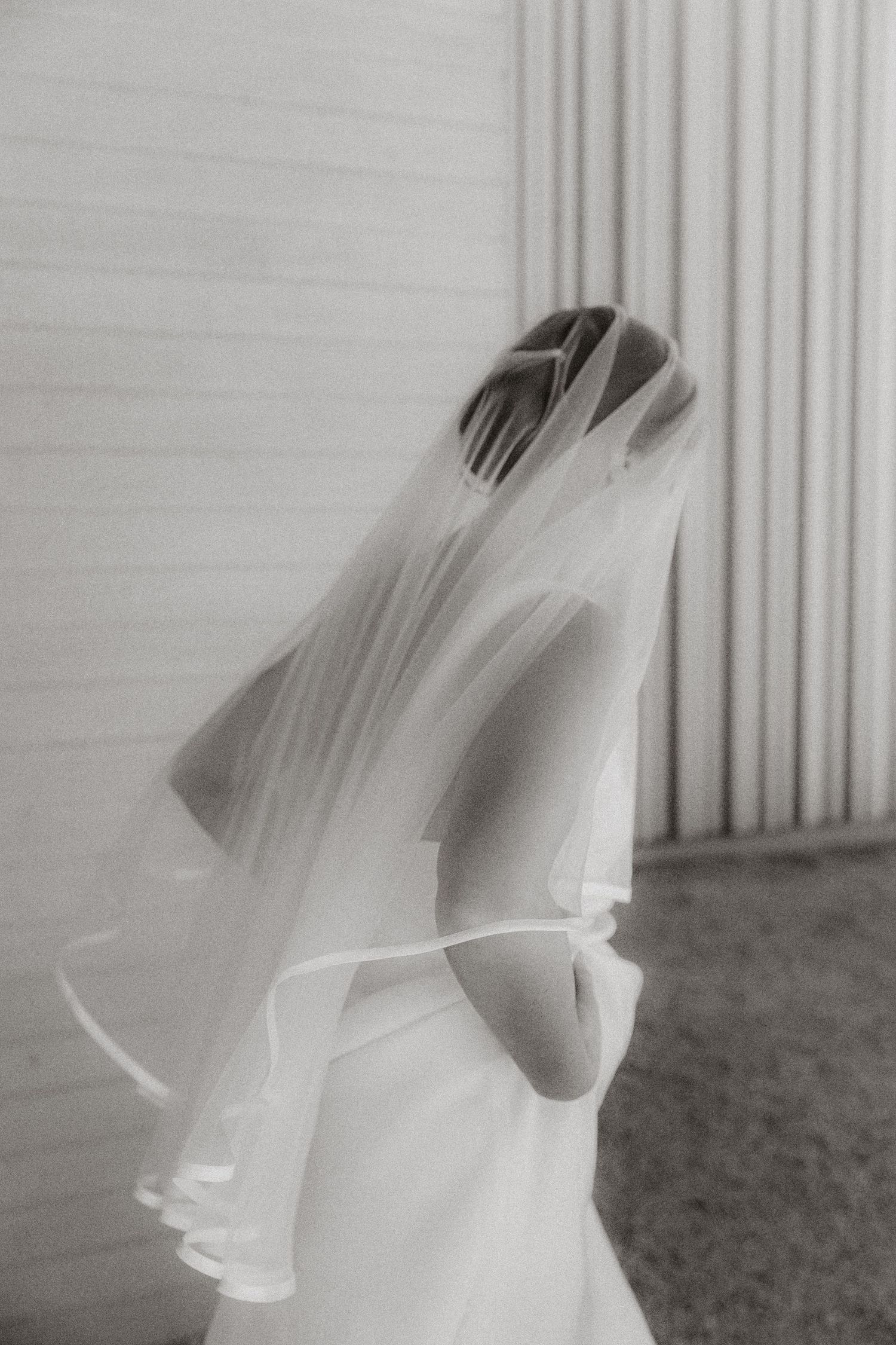 An artistic black and white photo of a flowing wedding veil against a striped wall.