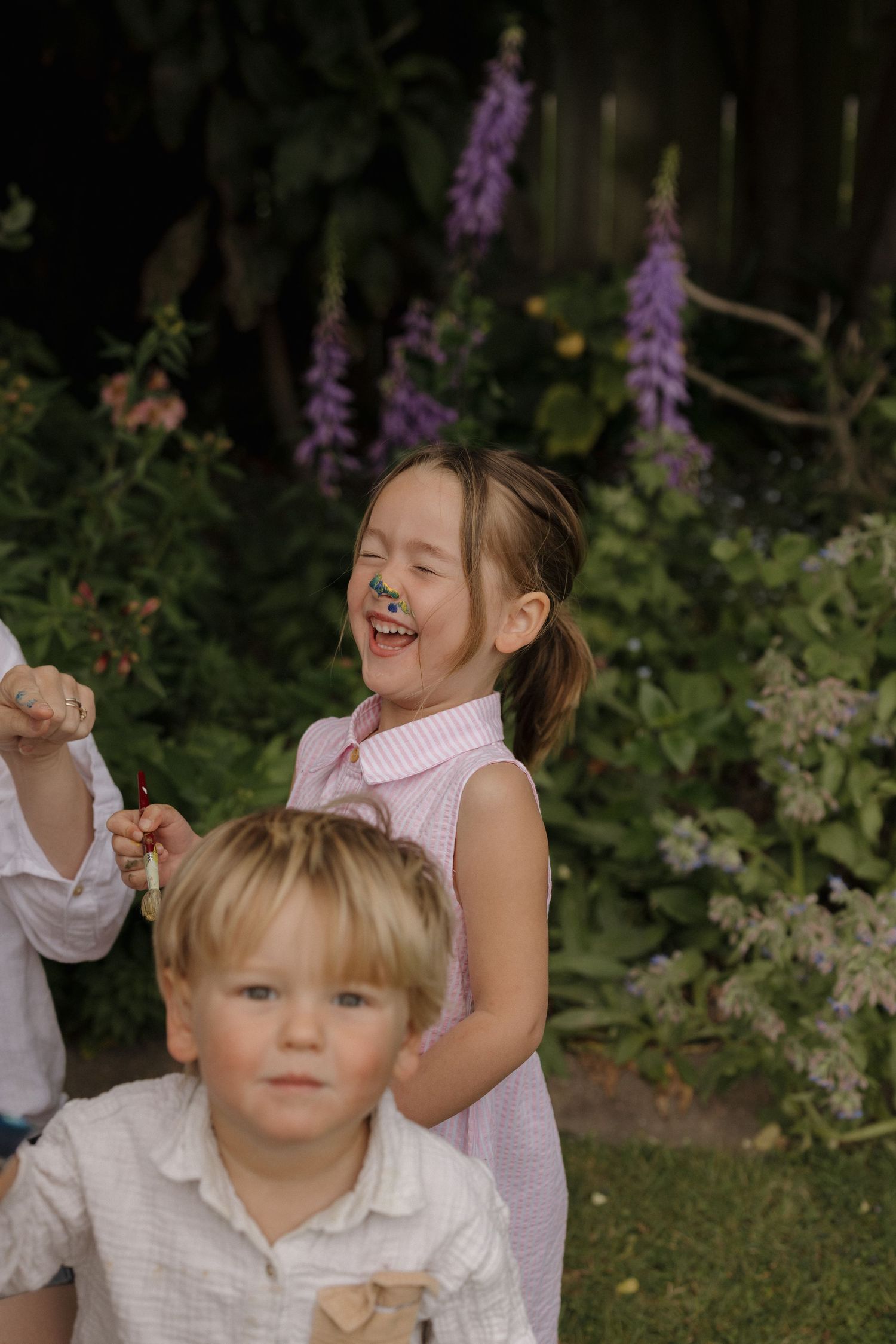 Children playing and laughing together in a garden with purple flowers blooming in the background.