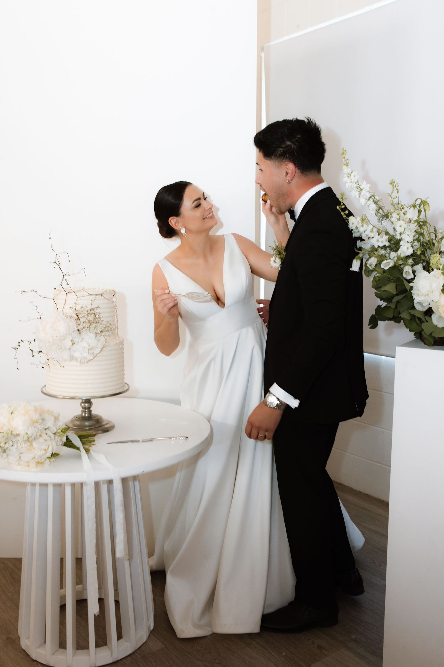 Elegant wedding scene with couple near white cake display and floral arrangements.