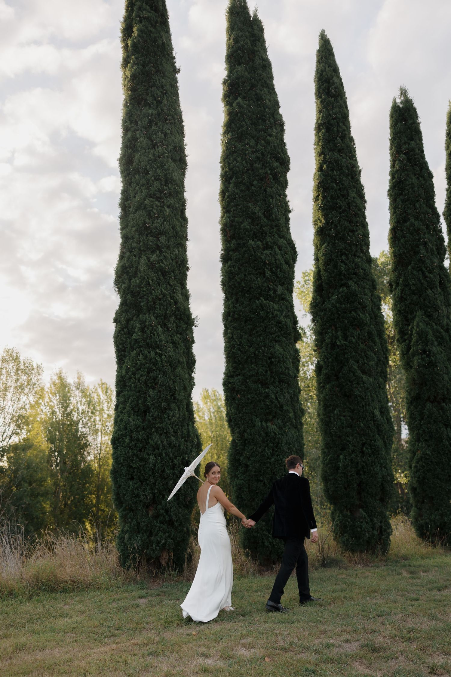 Dramatic wedding portrait scene with tall cypress trees creating a natural backdrop.