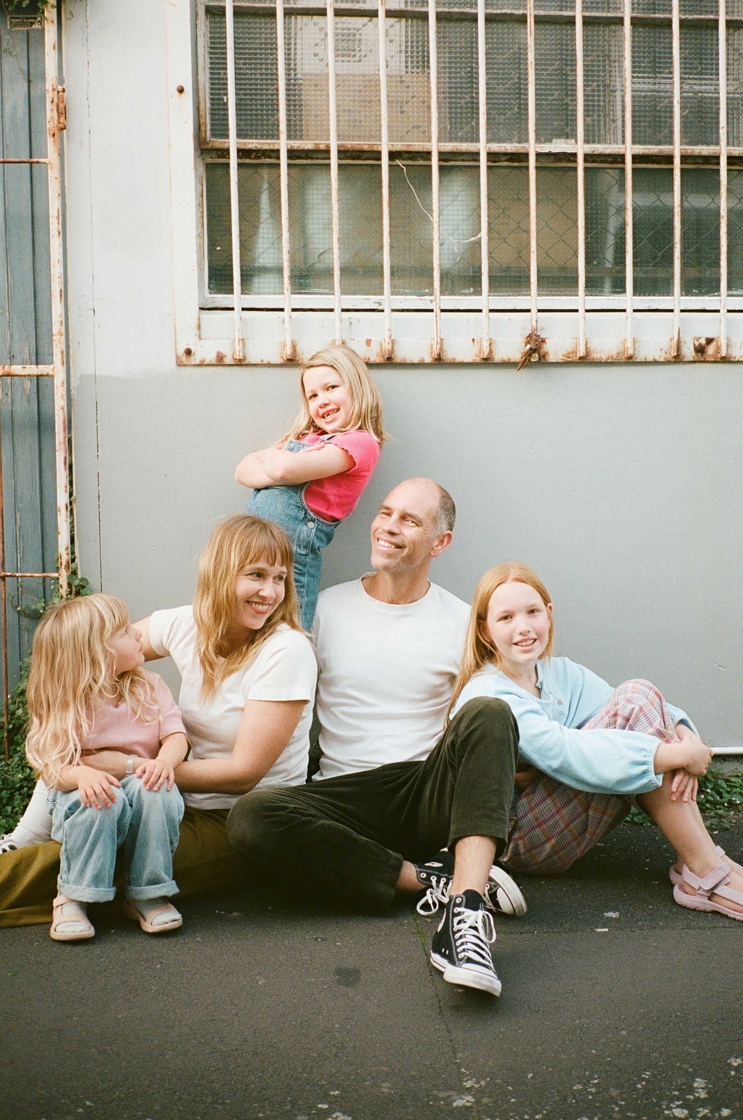 A happy family of five poses casually against a teal wall, smiling and laughing together outdoors.