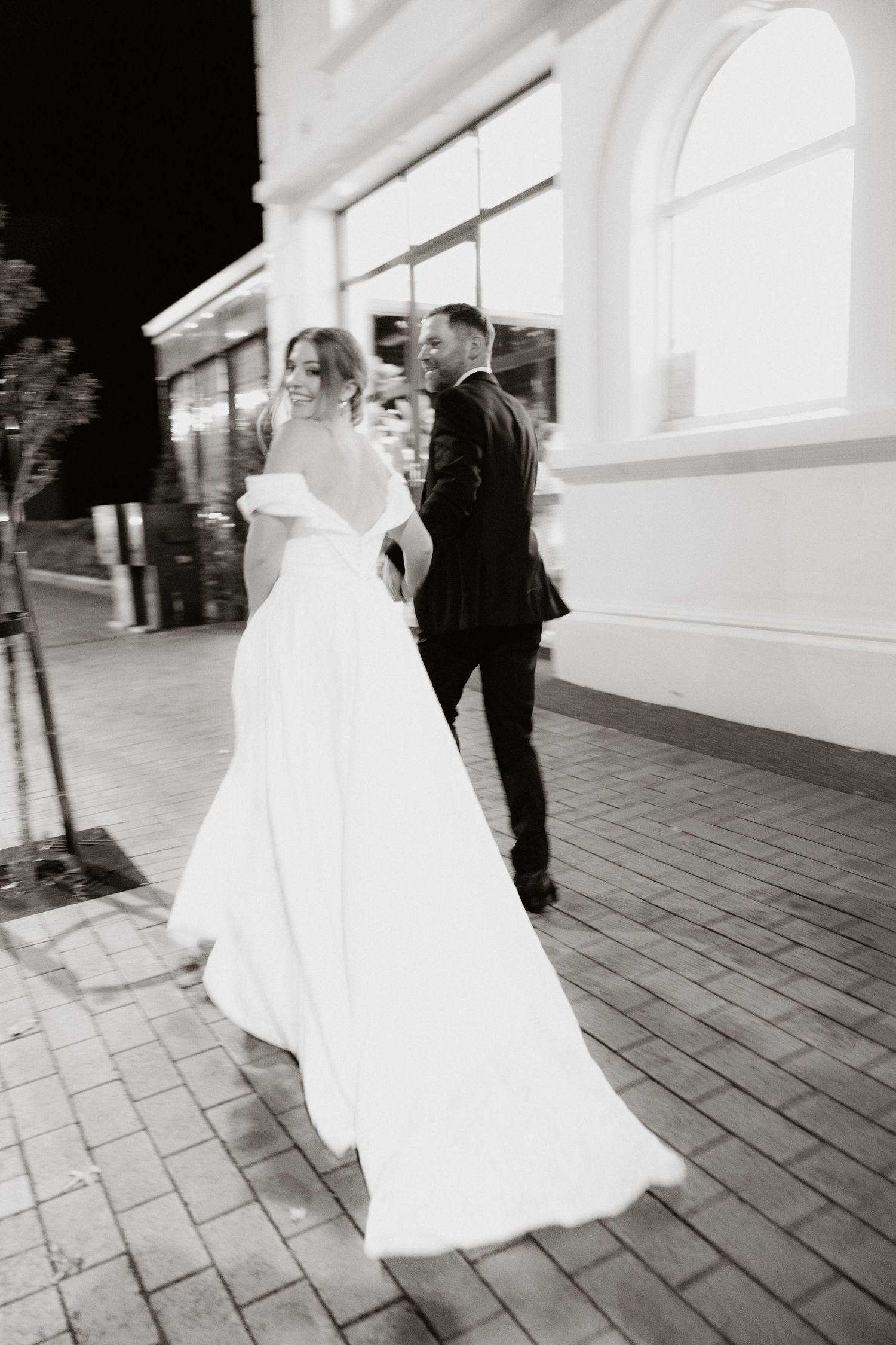 Wedding couple walking along white building exterior with flowing dress.