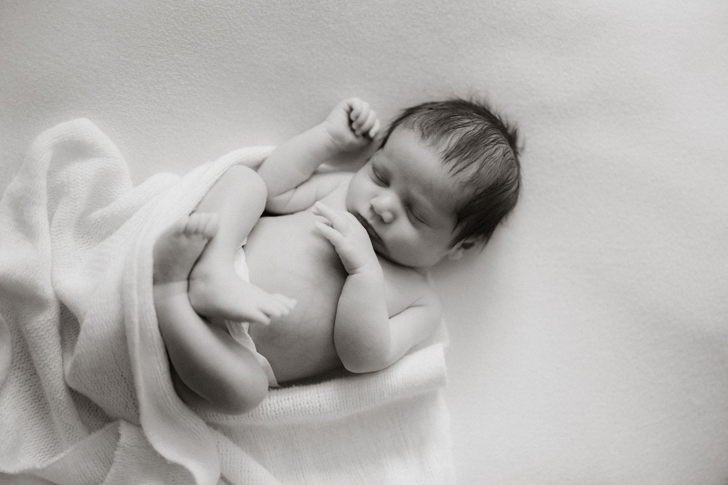 Peaceful black and white portrait of sleeping newborn partially wrapped in white fabric.