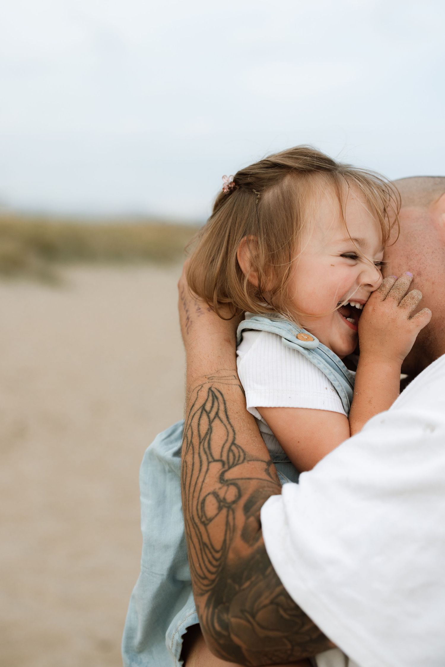 Sweet candid moment captured on beach showing playful affection between parent and child in soft natural light.